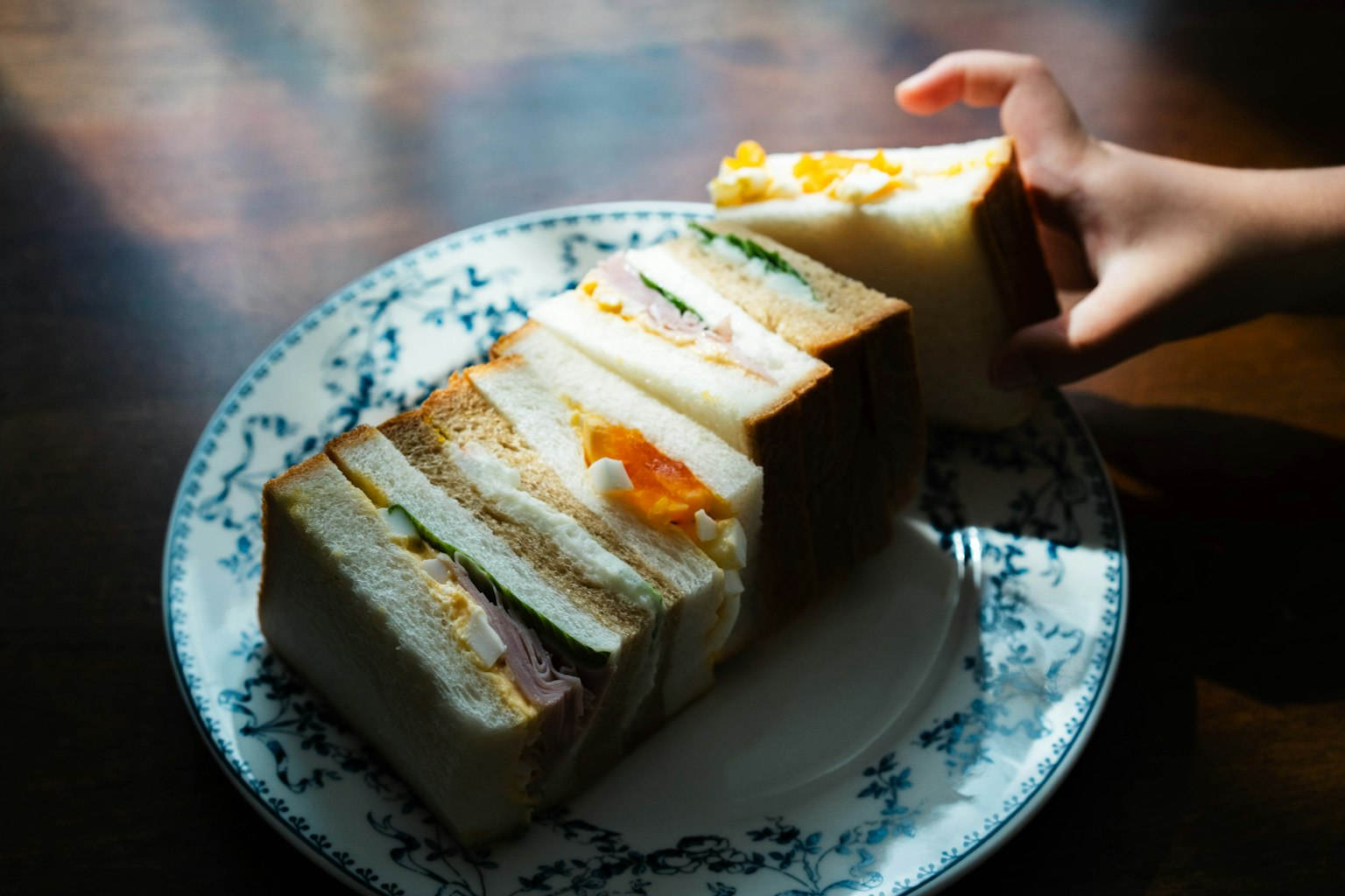 Una mano che raggiunge un panino a strati su un piatto decorativo