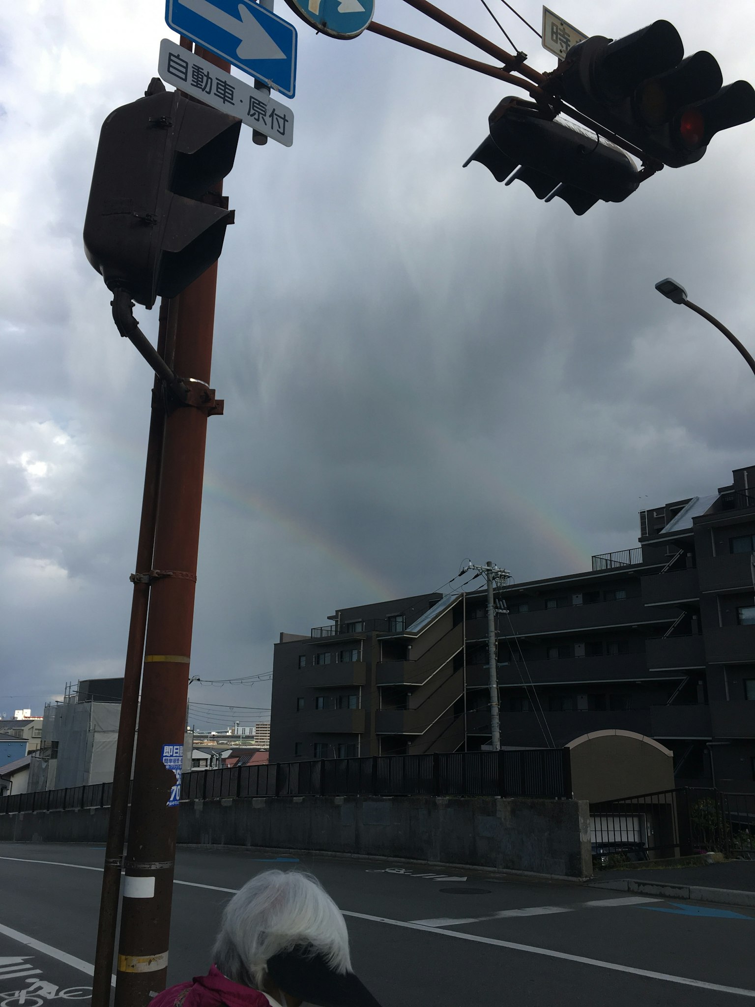 Scène de rue avec un feu de circulation et des bâtiments sous un ciel nuageux avec un arc-en-ciel