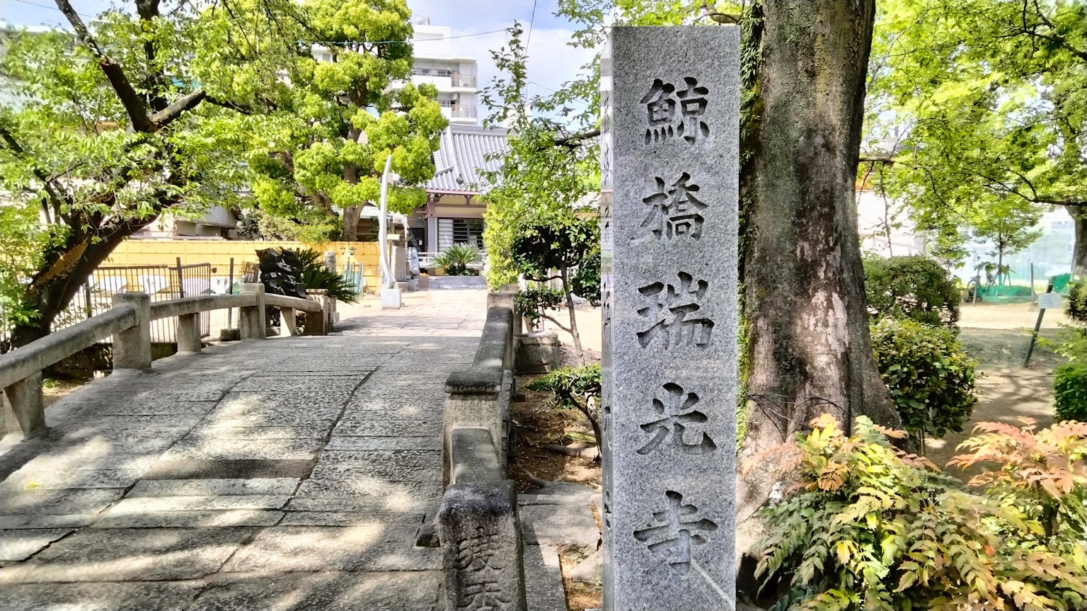 Stone sign near a bridge surrounded by lush greenery under a bright sky