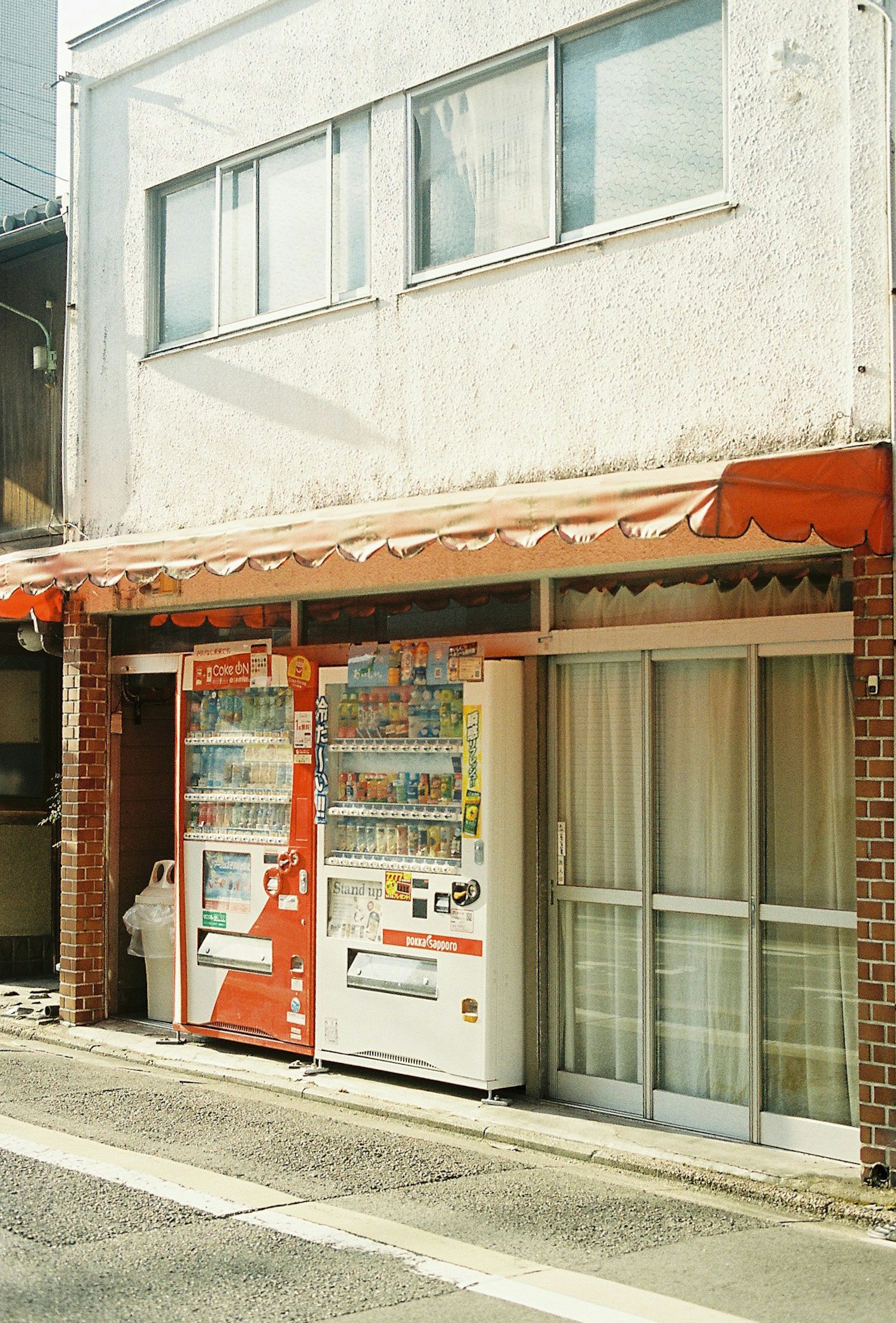 兩台自動販賣機在一個有橙色遮陽篷的建築前