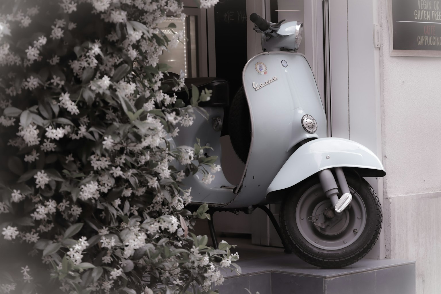 A vintage blue scooter partially hidden by white flowers