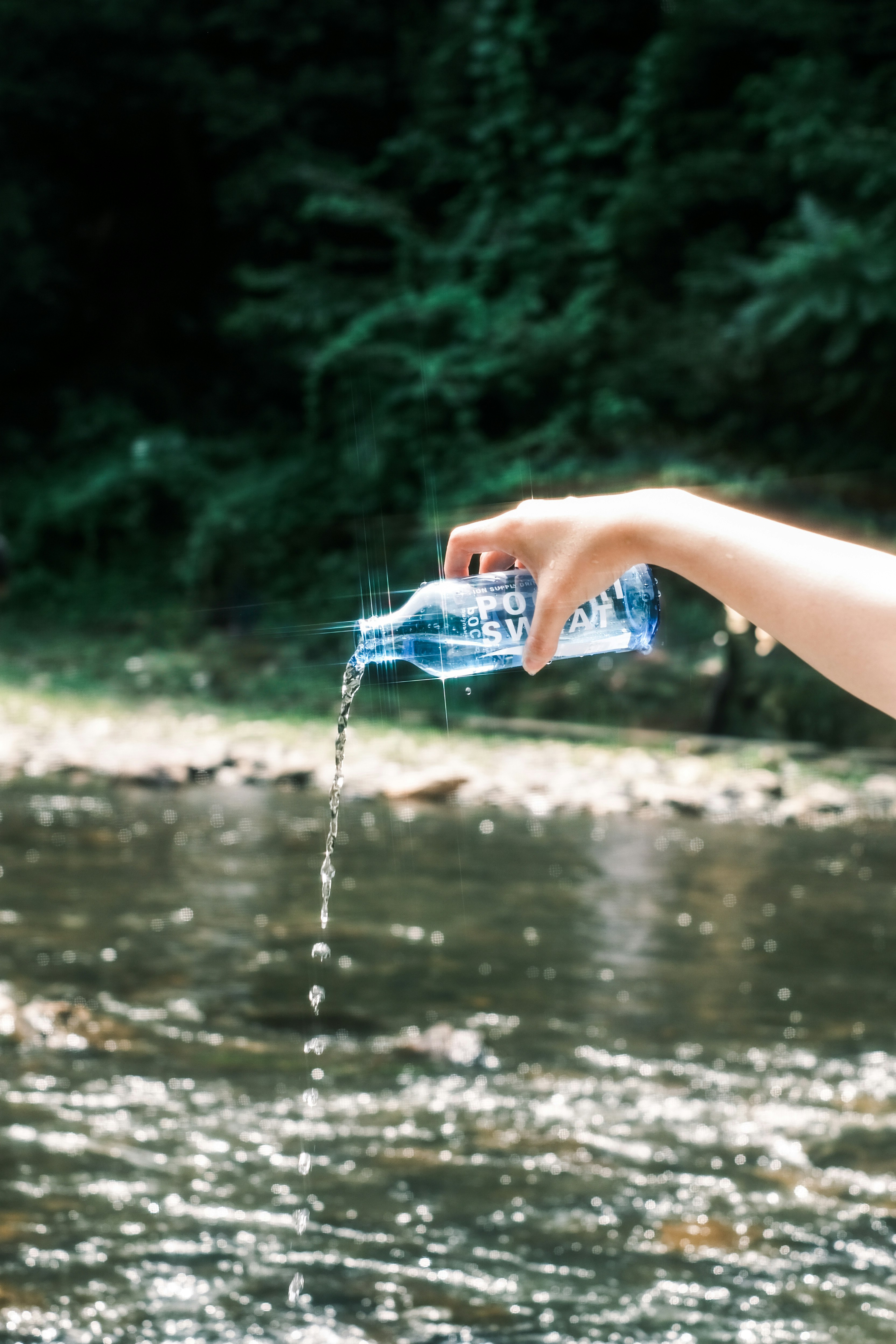 Szenenmotiv für ein Sommergetränk: Wasser wird aus der Hand am Flussrand gegossen