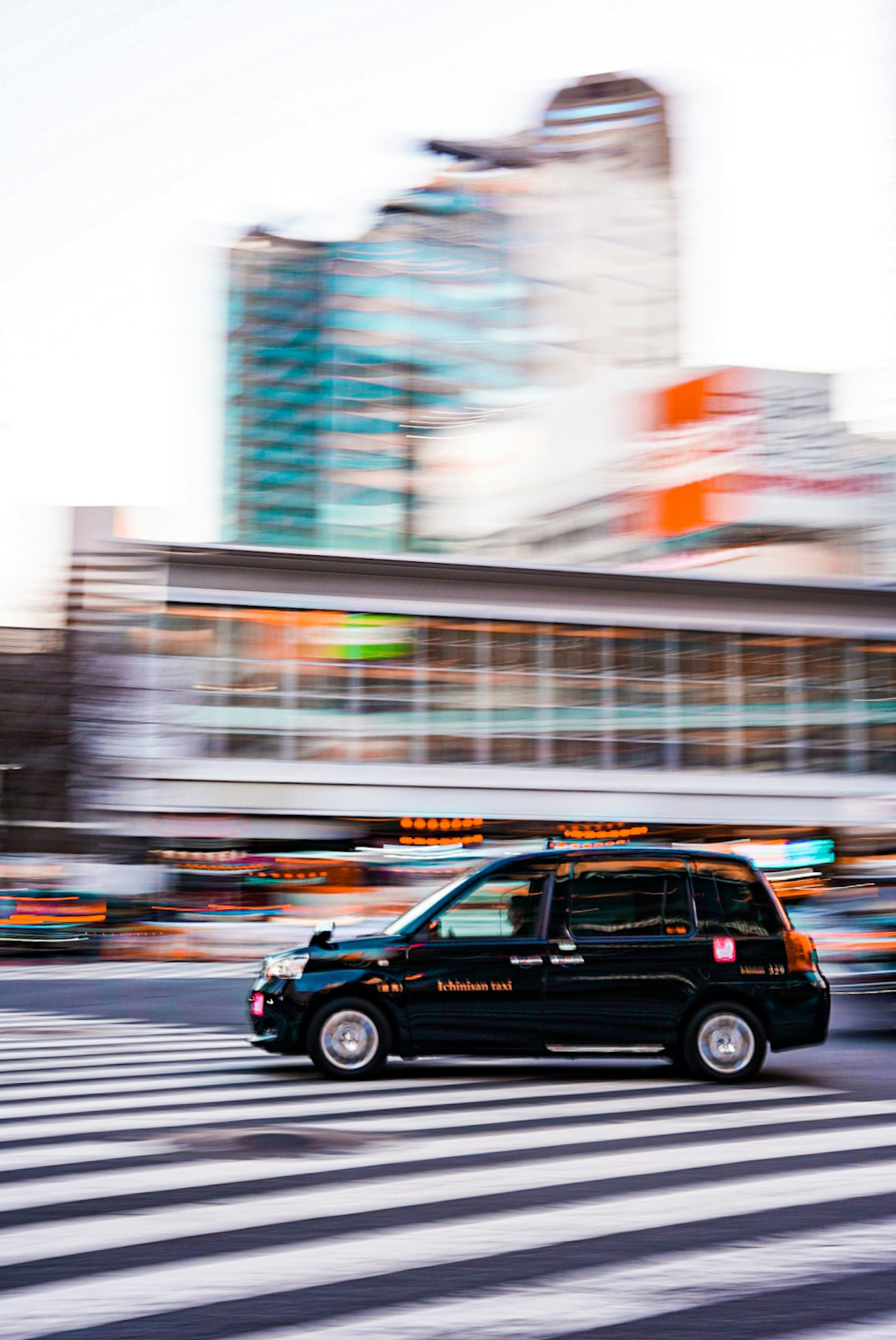 Un taxi noir accélérant à travers un passage piéton avec un arrière-plan urbain flou
