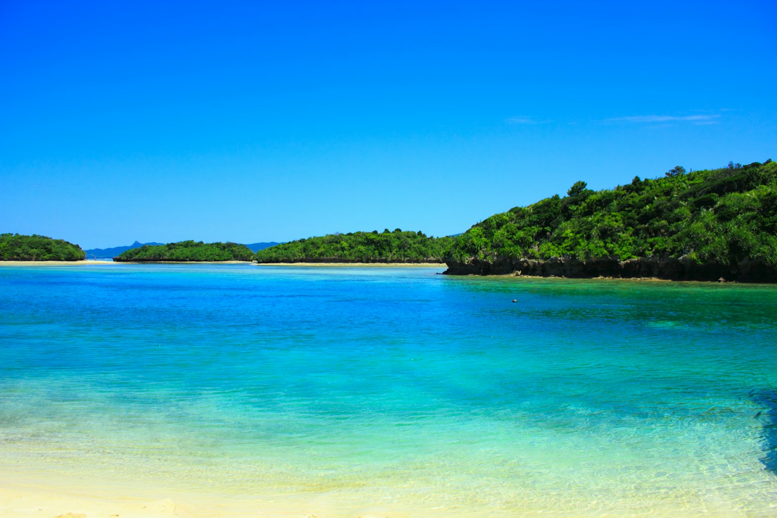 Vista de playa escénica con cielo azul y agua turquesa clara rodeada de islas verdes