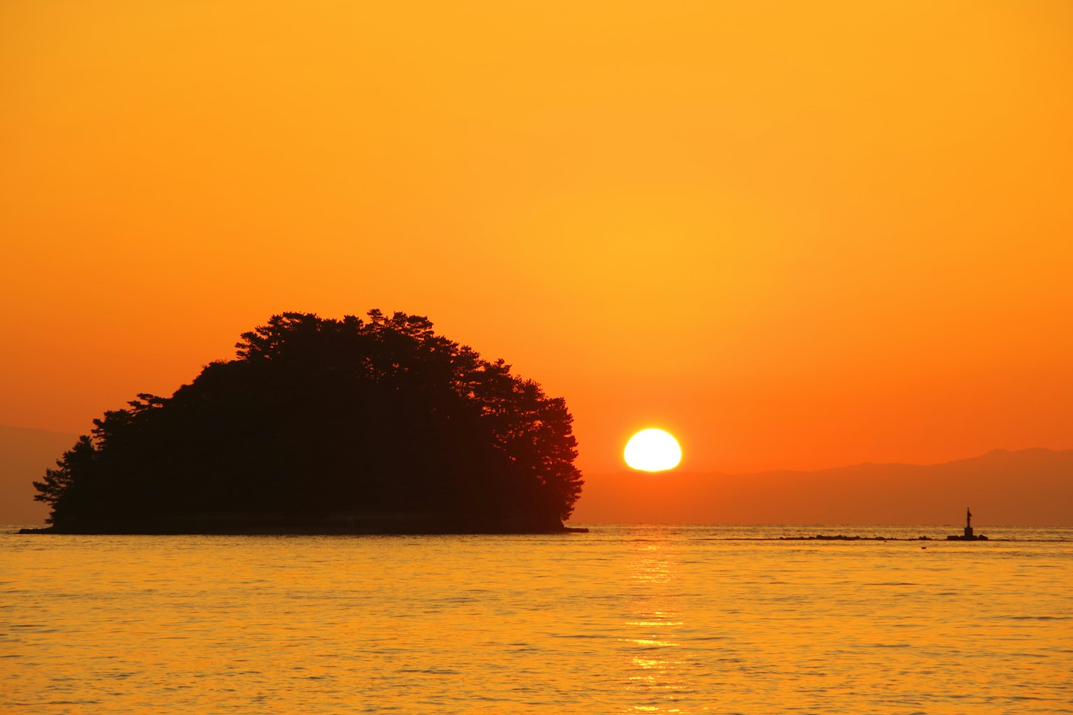Ein ruhiger Ozean bei Sonnenuntergang mit einer Inselsilhouette