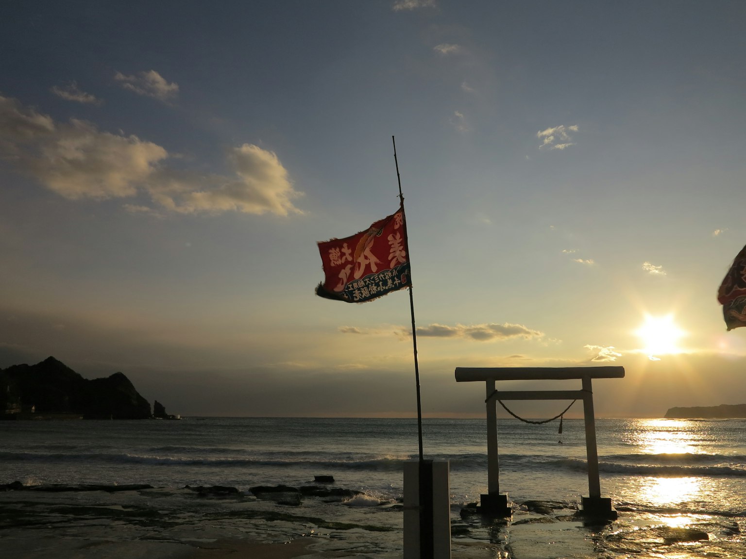 ประตูโทริอิและธงแดงที่ชายหาดยามพระอาทิตย์ตก