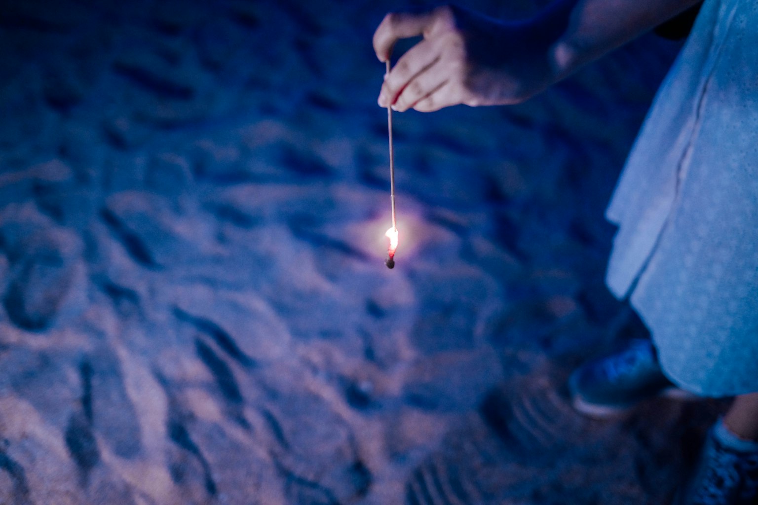 Gros plan d'une main tenant une étincelle sur la plage dans une lumière bleue avec l'étincelle vacillante