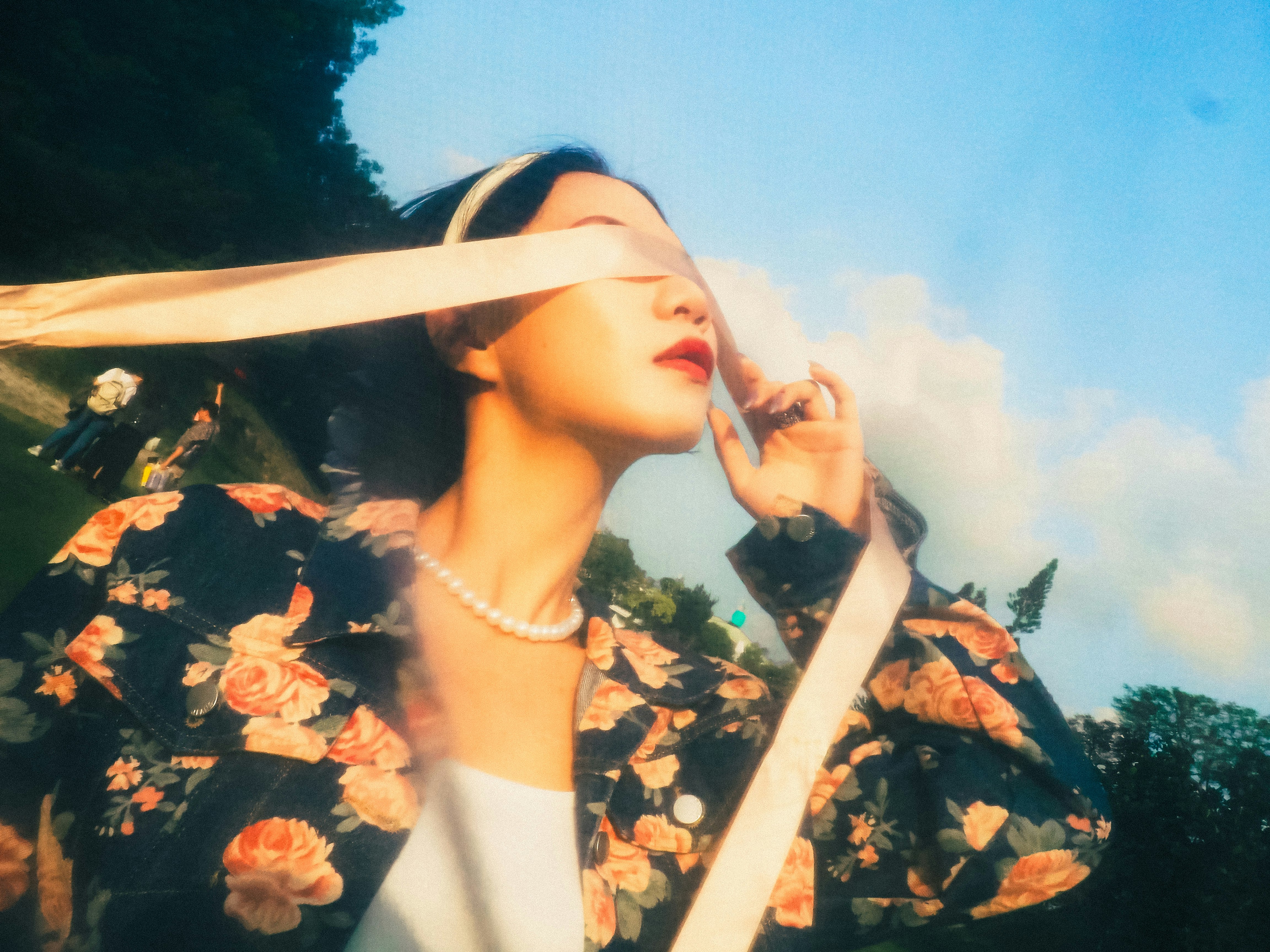 花柄の服を着た女性が青空の下で目を覆うリボンをしている