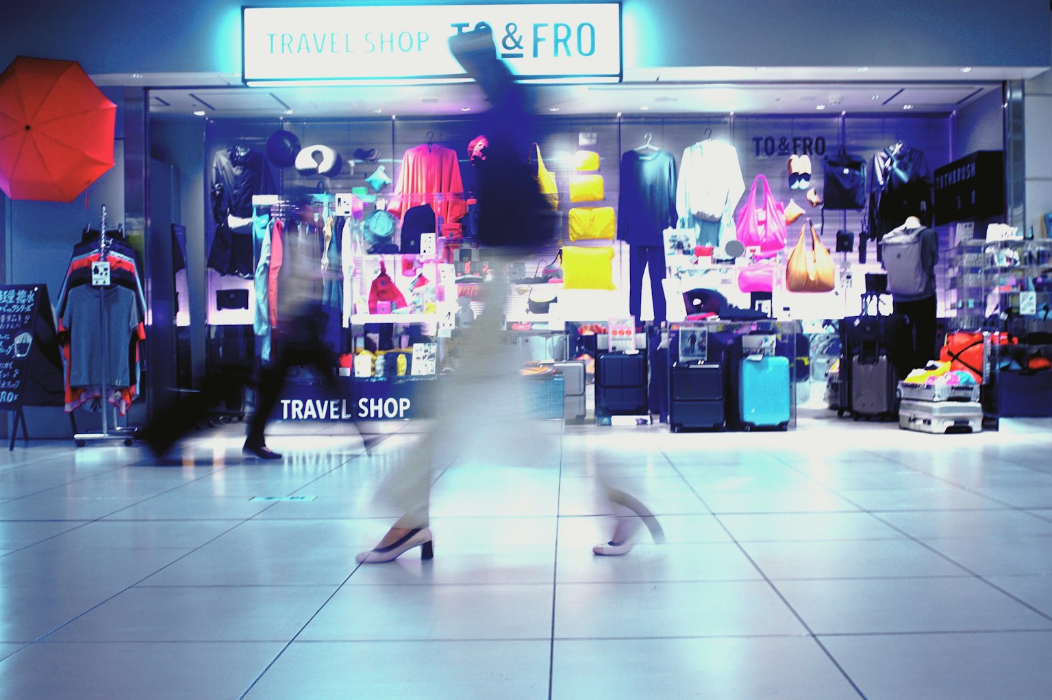 Una vetrina di centro commerciale affollata con merce colorata e figure sfocate di persone
