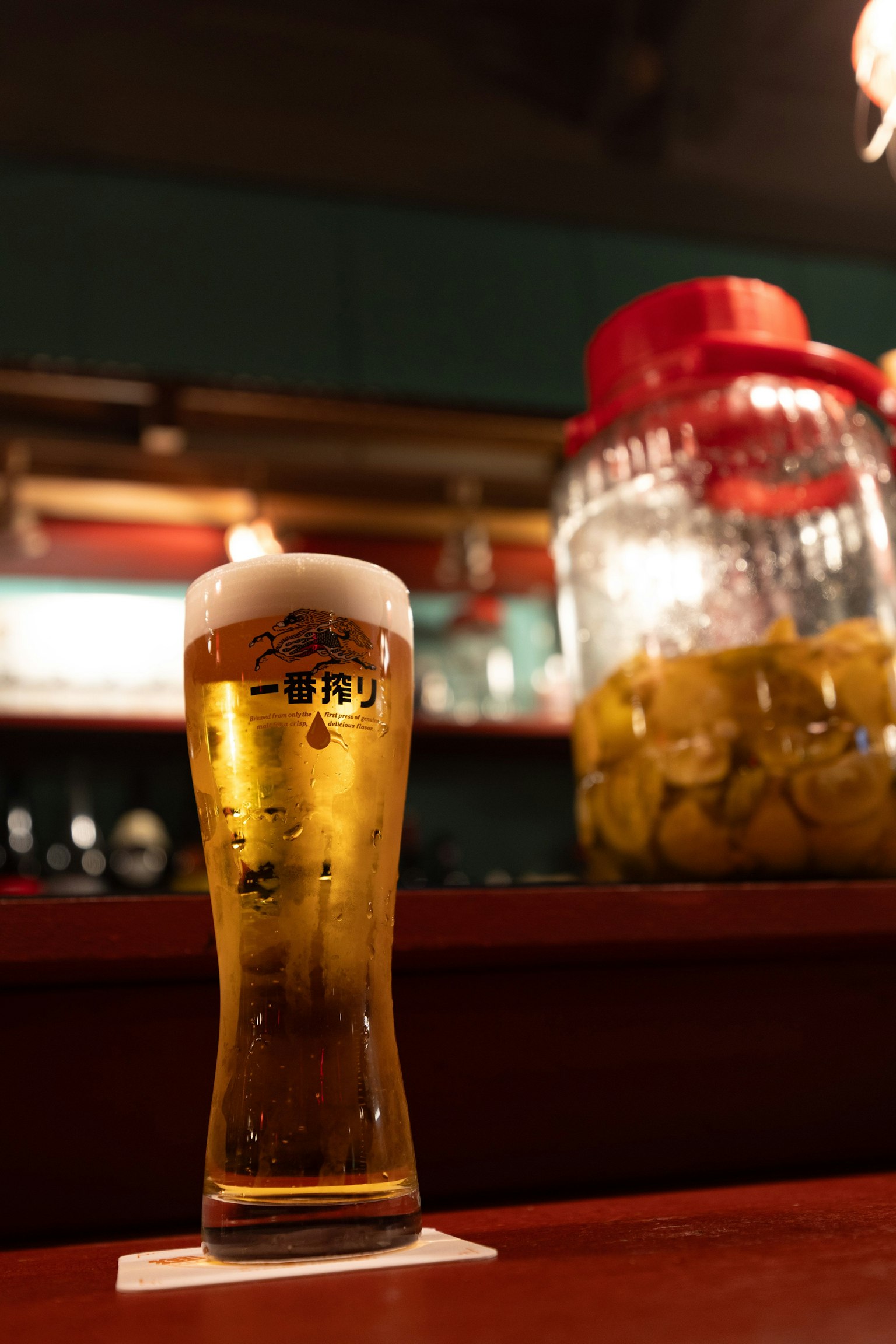 Un verre de bière sur un comptoir de bar avec un grand pot de fruits en arrière-plan