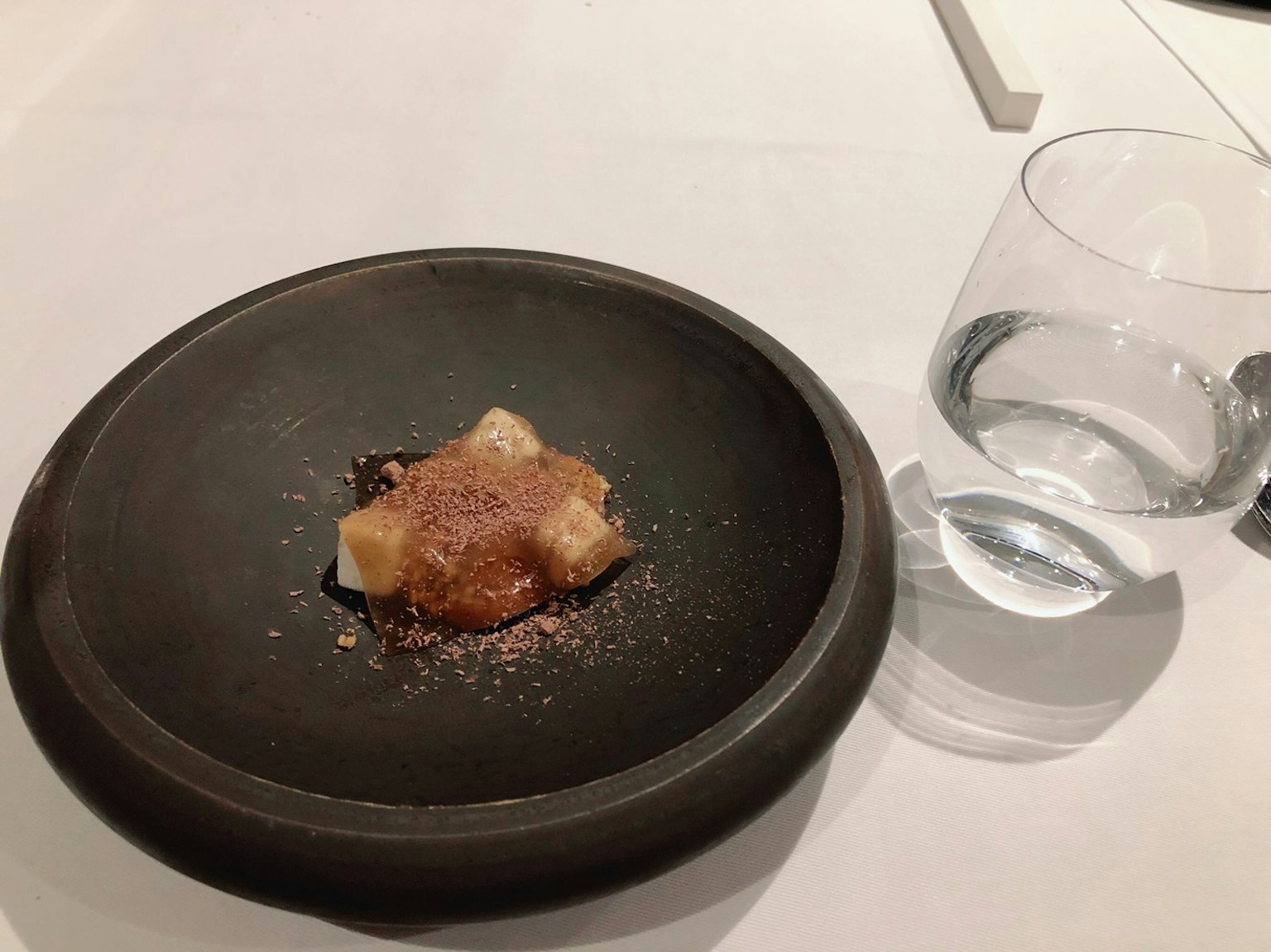Dessert auf einem schwarzen Teller mit einem Glas Wasser serviert