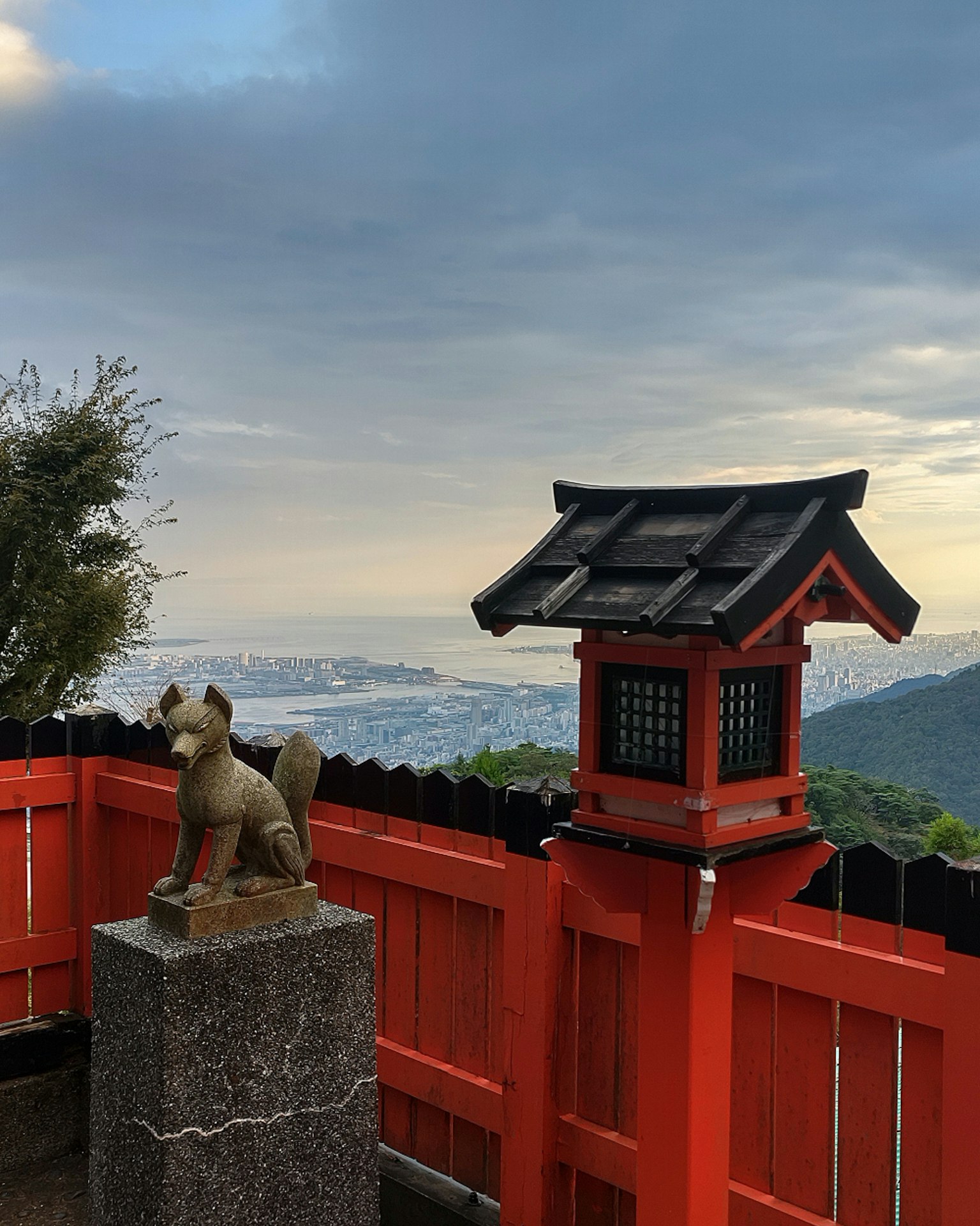 风景如画的景观，石台上的狐狸雕像和小型传统屋顶的灯笼，背景是山丘