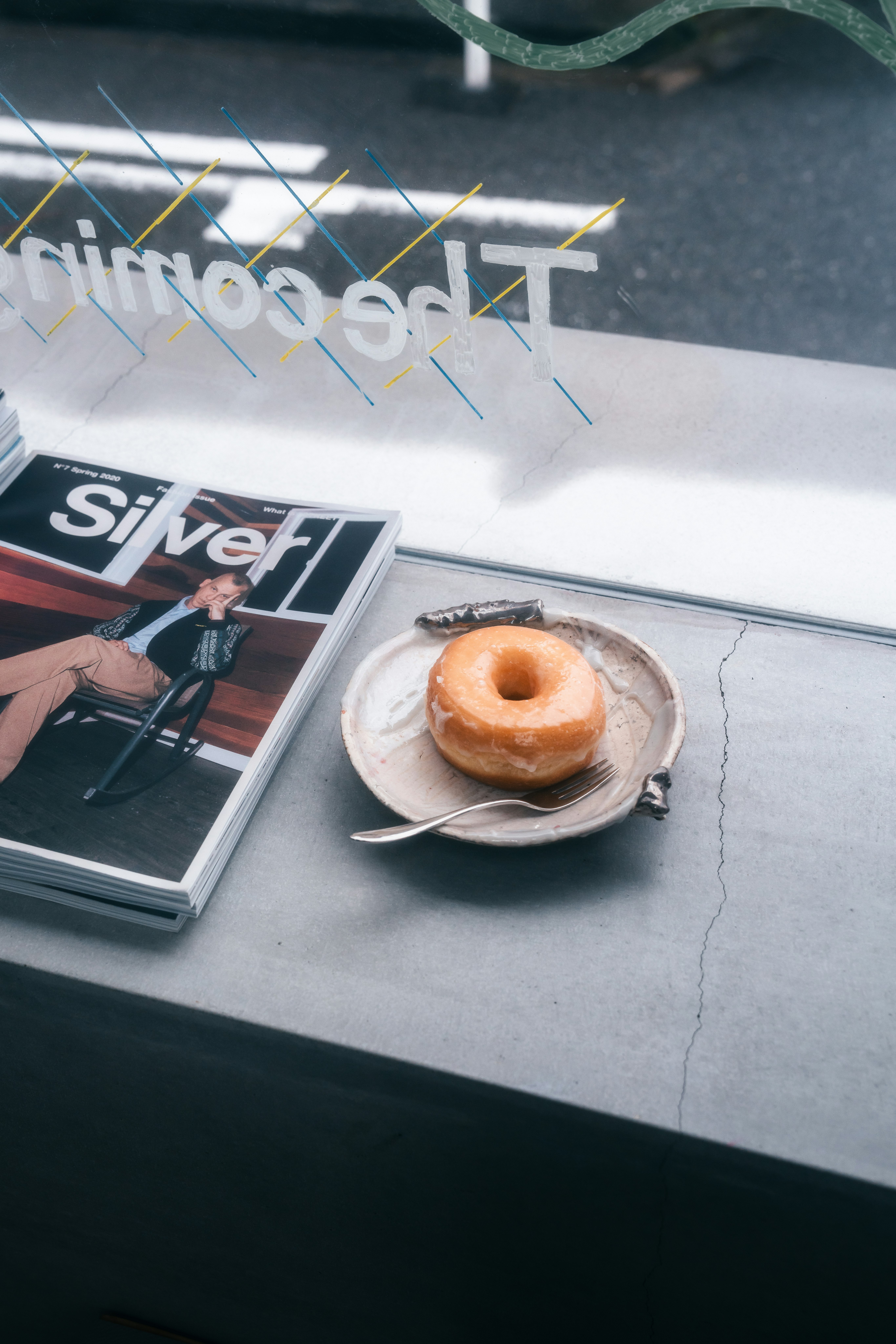A cafe table with a donut on a plate and an open magazine