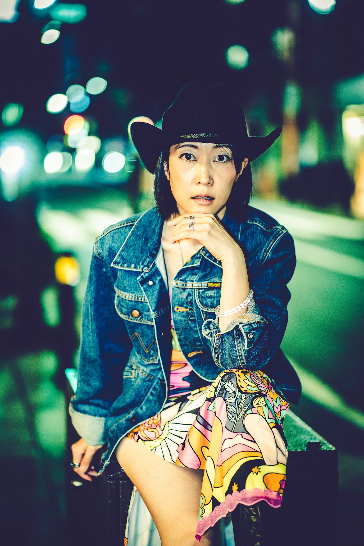 Une femme portant une veste en jean et un chapeau de cow-boy assise dans la rue la nuit