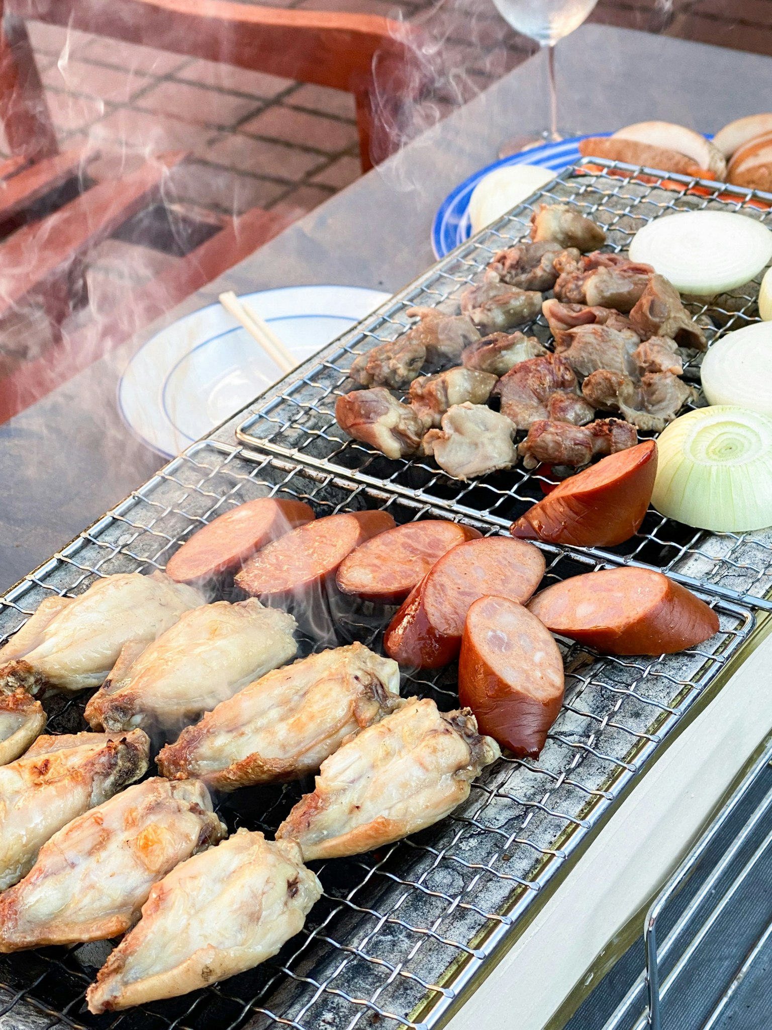 바베큐 그릴에 치킨 윙, 소시지, 야채가 있는 사진