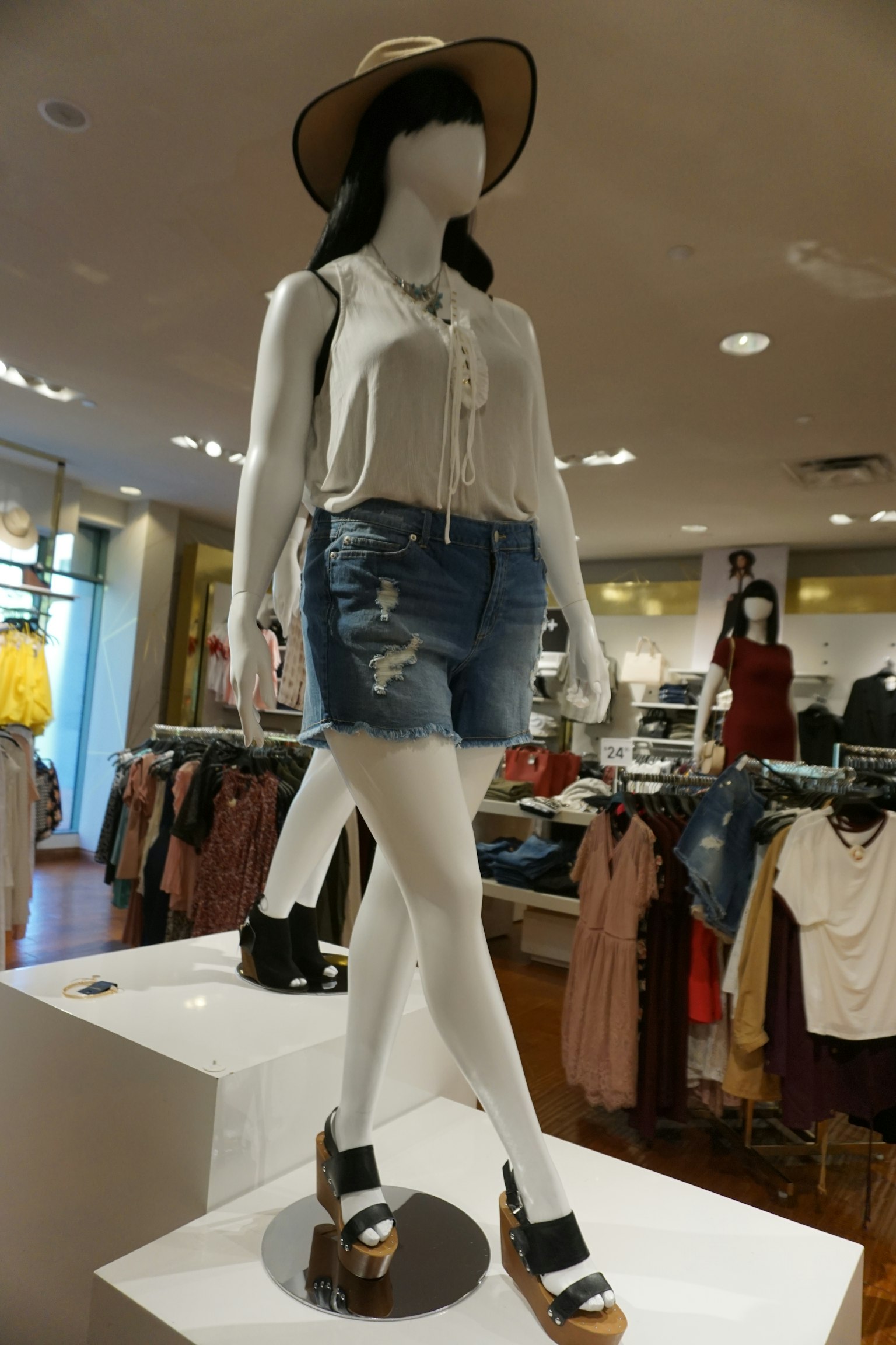 A mannequin wearing a white blouse and denim shorts with a hat