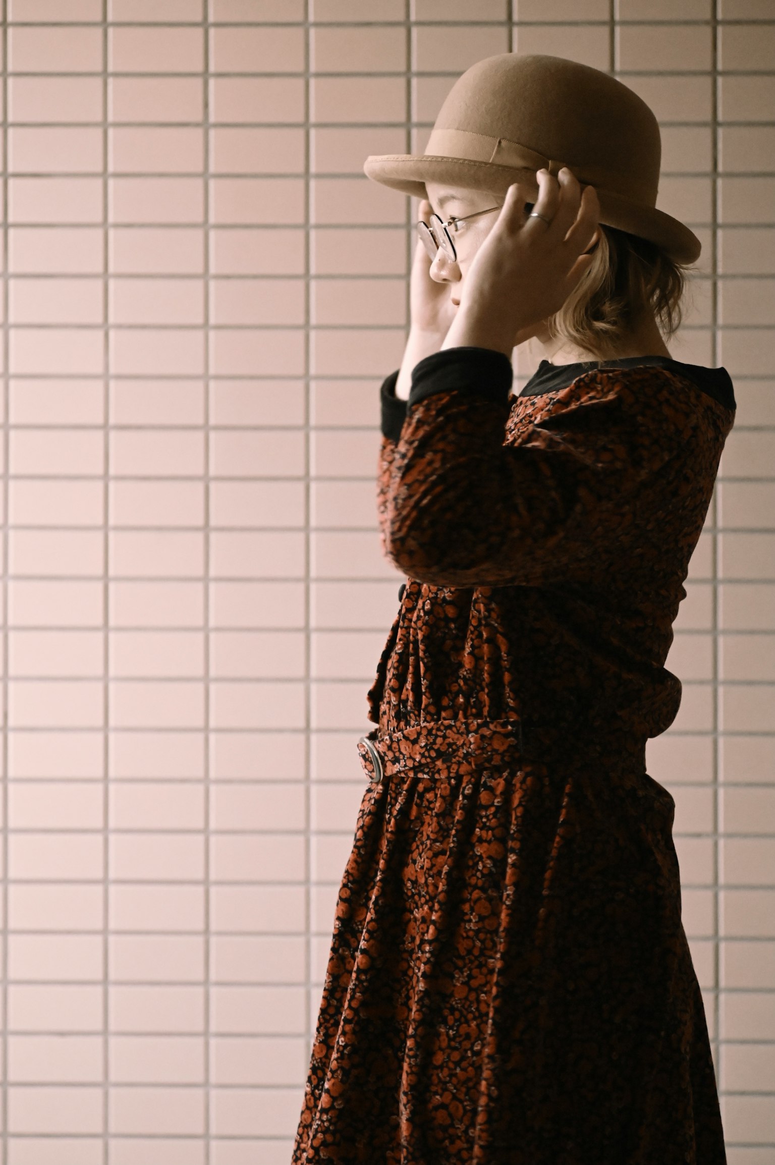 A girl in a brown dress wearing a bowler hat covering her face with her hands