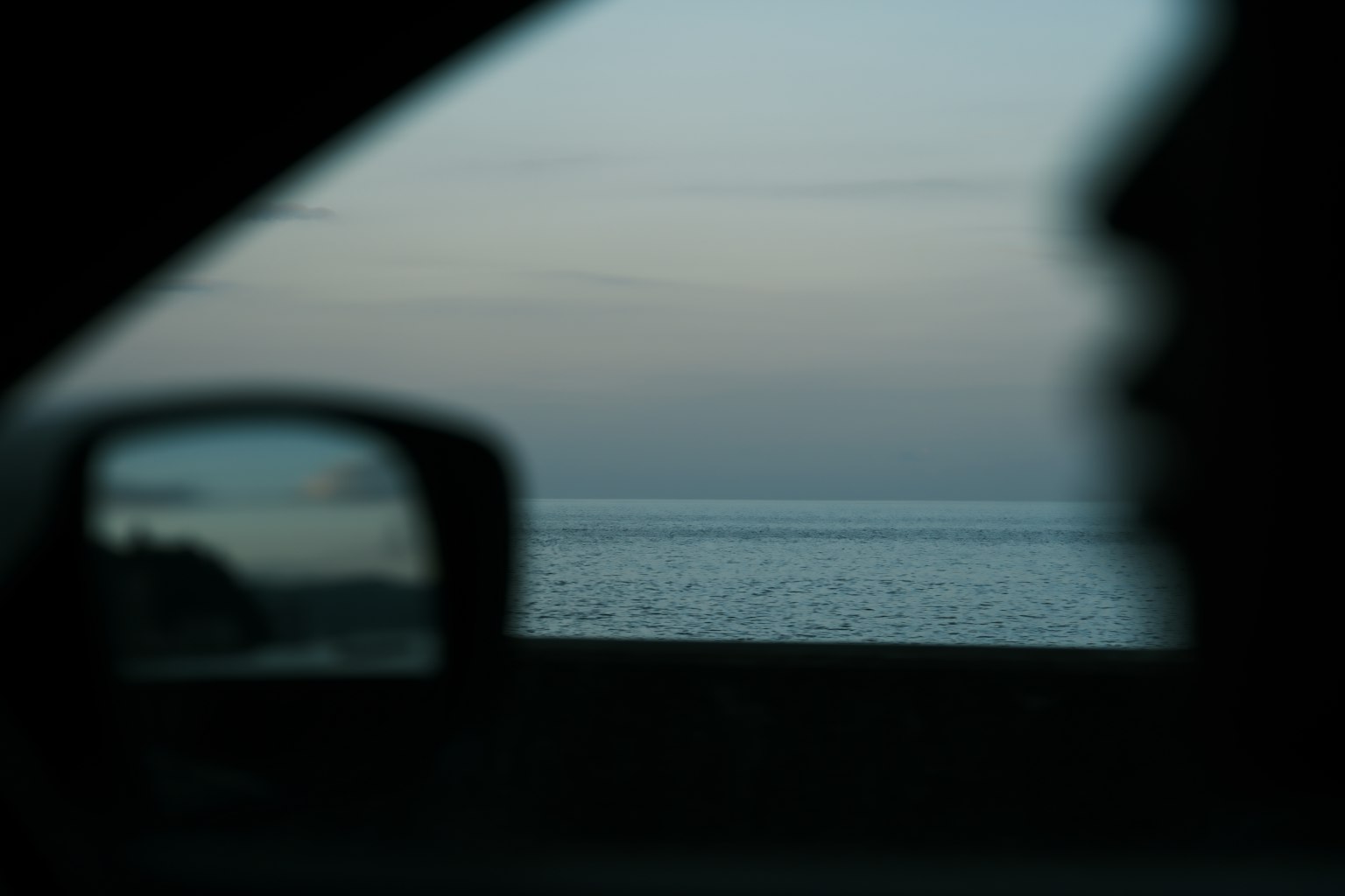 View of the sea at dusk from a car window with a blurred silhouette