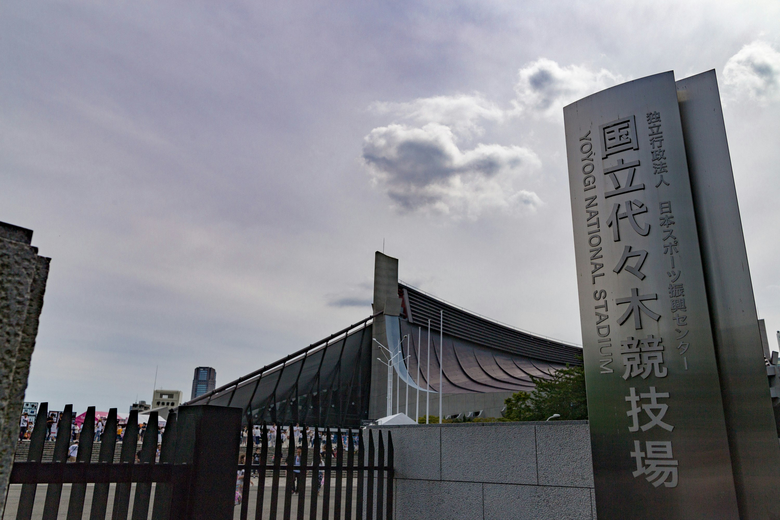 多雲天空下的場館入口，豎立「Yoyogi National Technical Stadium」標牌