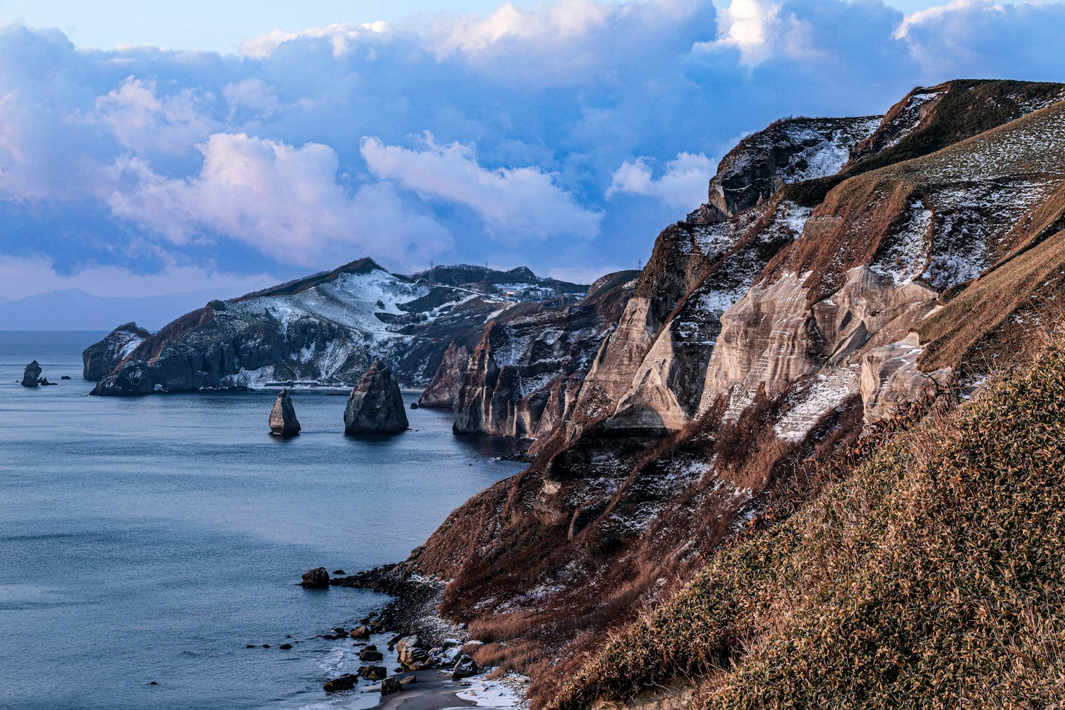 Acantilados cubiertos de nieve y paisaje marino tranquilo con nubes dramáticas y formaciones rocosas