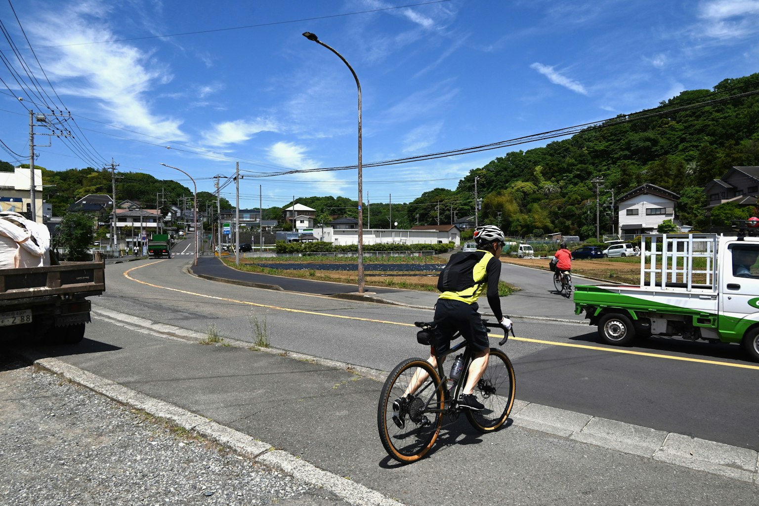 Một người đàn ông đang đi xe đạp trên đường với cây xanh và bầu trời xanh phía sau