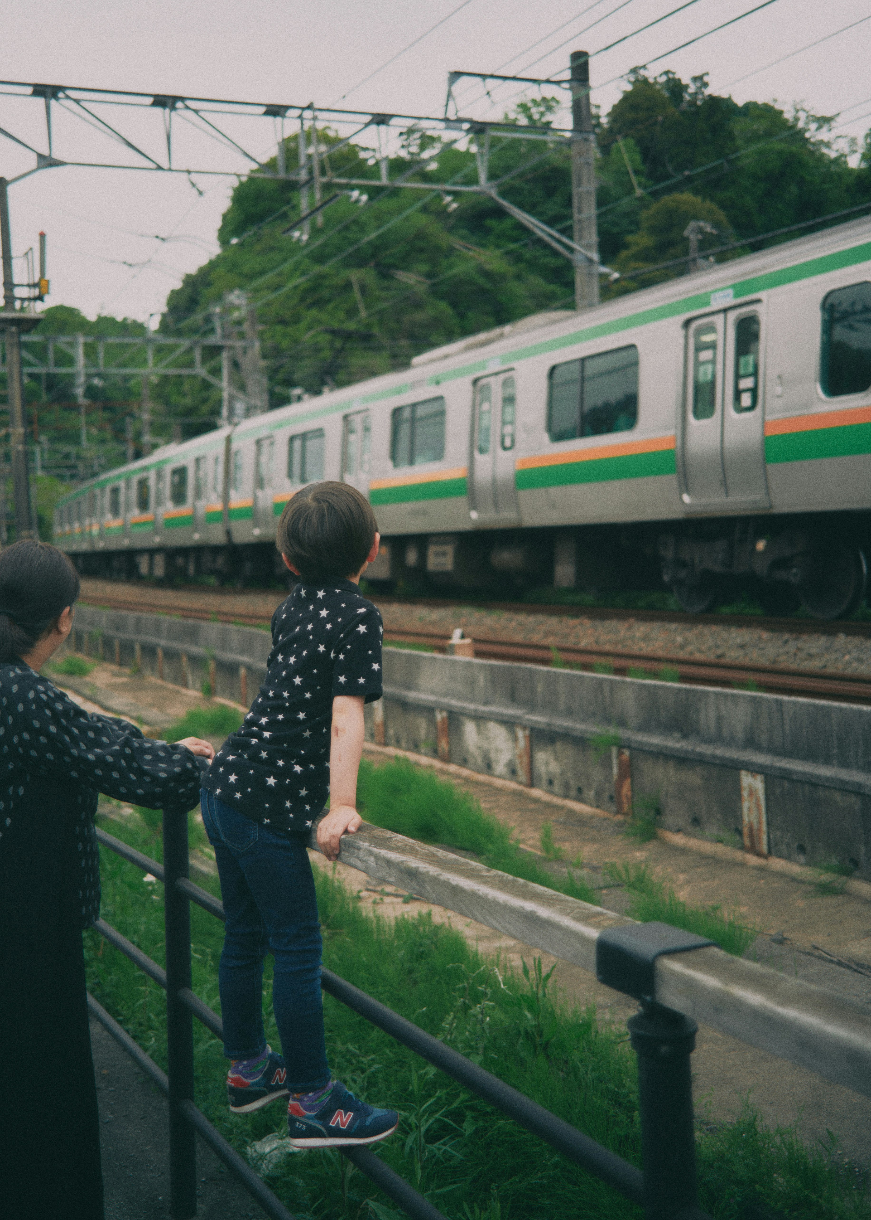 線路沿いの電車を見つめる親子の後ろ姿