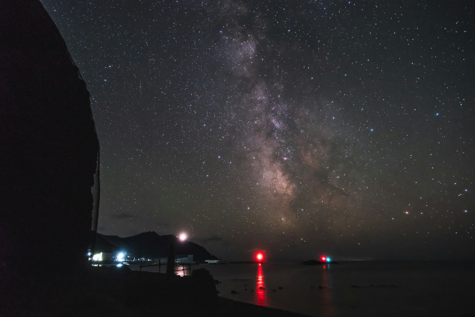 美麗的星空和銀河海岸景色 紅色燈塔的光在水面上反射