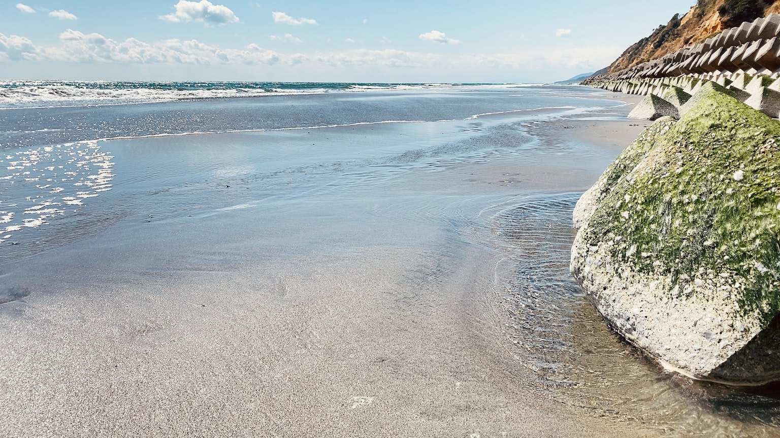Vista panoramica della spiaggia con onde leggere, costa rocciosa, cielo blu e nuvole