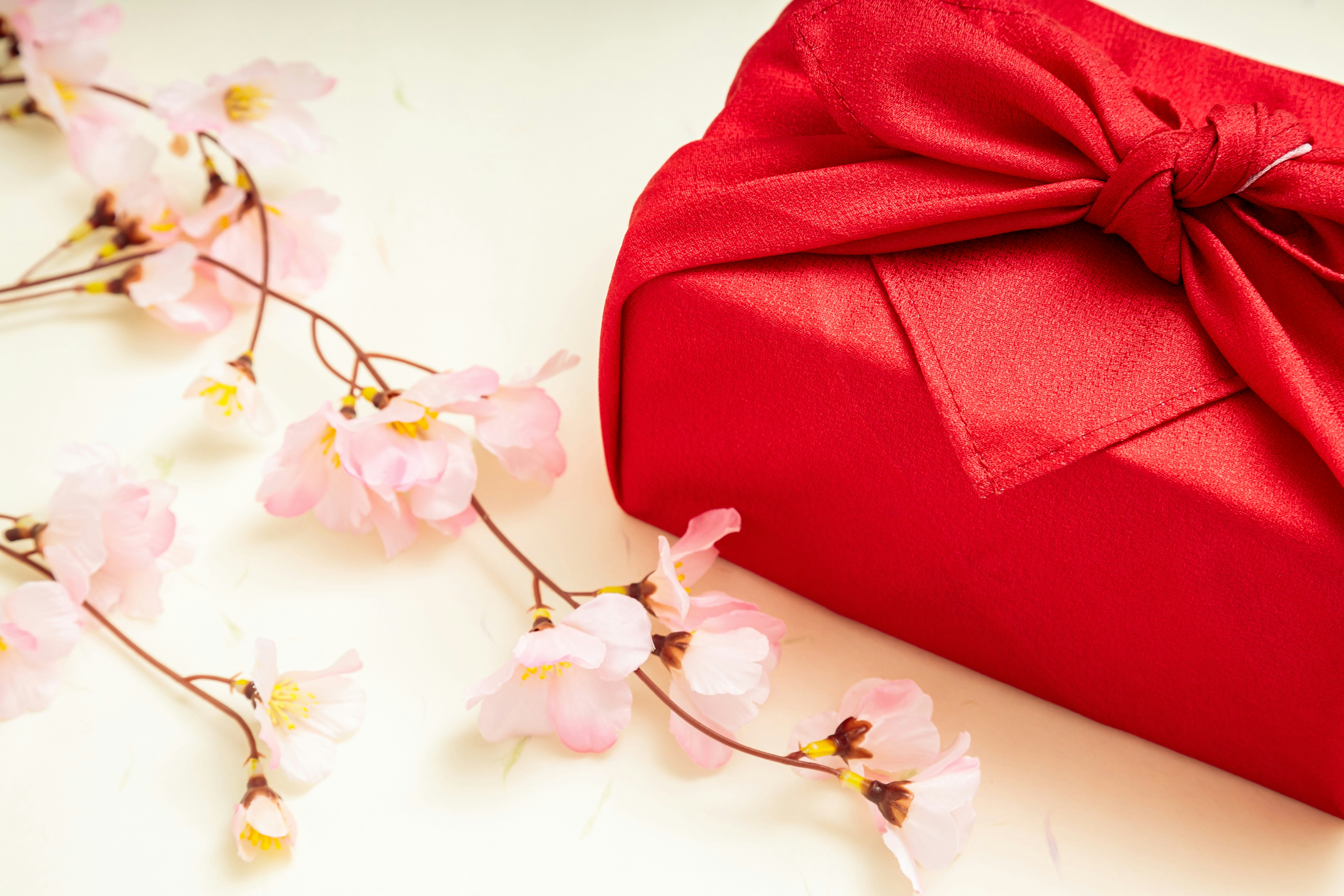 赤い風呂敷包みと桜の花飾りのある贈り物の画像