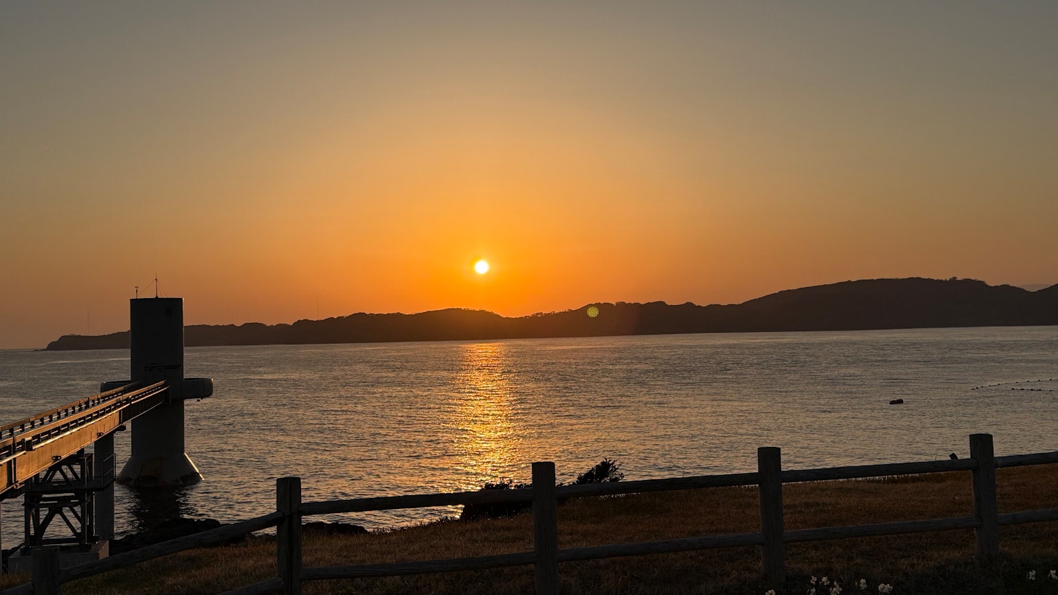 Un bel tramonto sul mare con un molo e colline sullo sfondo