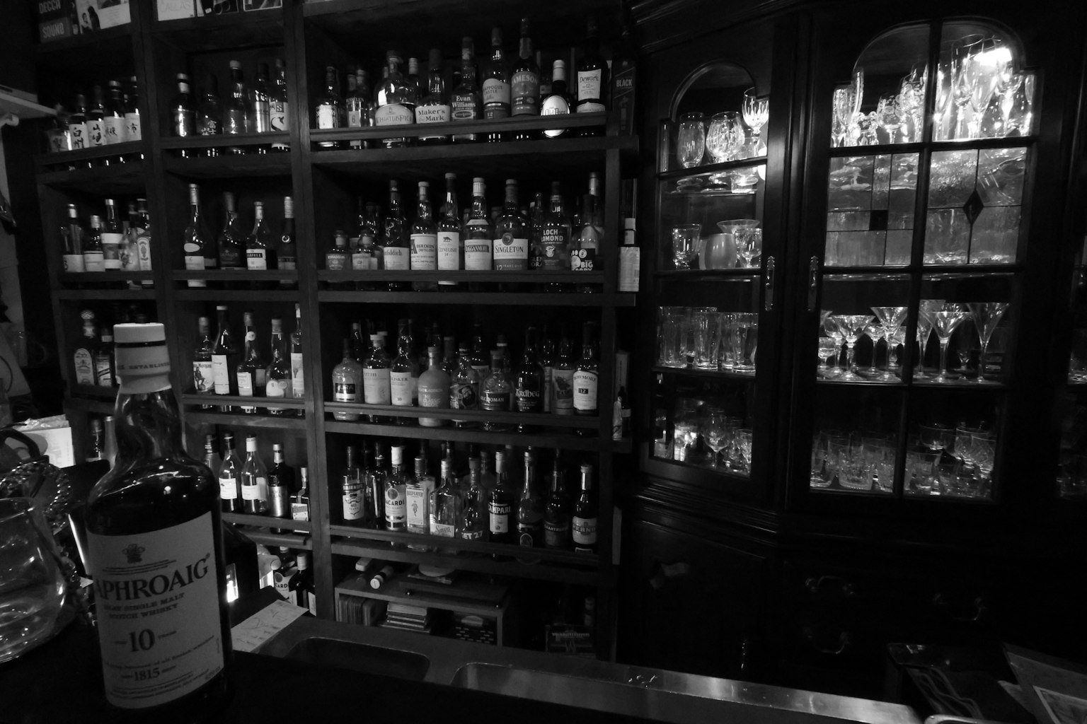 Una estantería de bar en blanco y negro llena de diversas botellas y cristalería