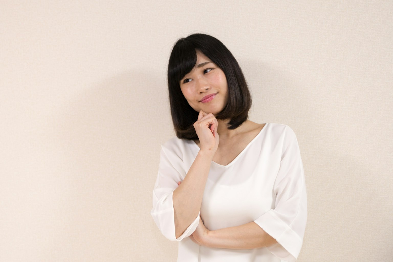 A woman in a white top appears to be deep in thought against a light-colored background