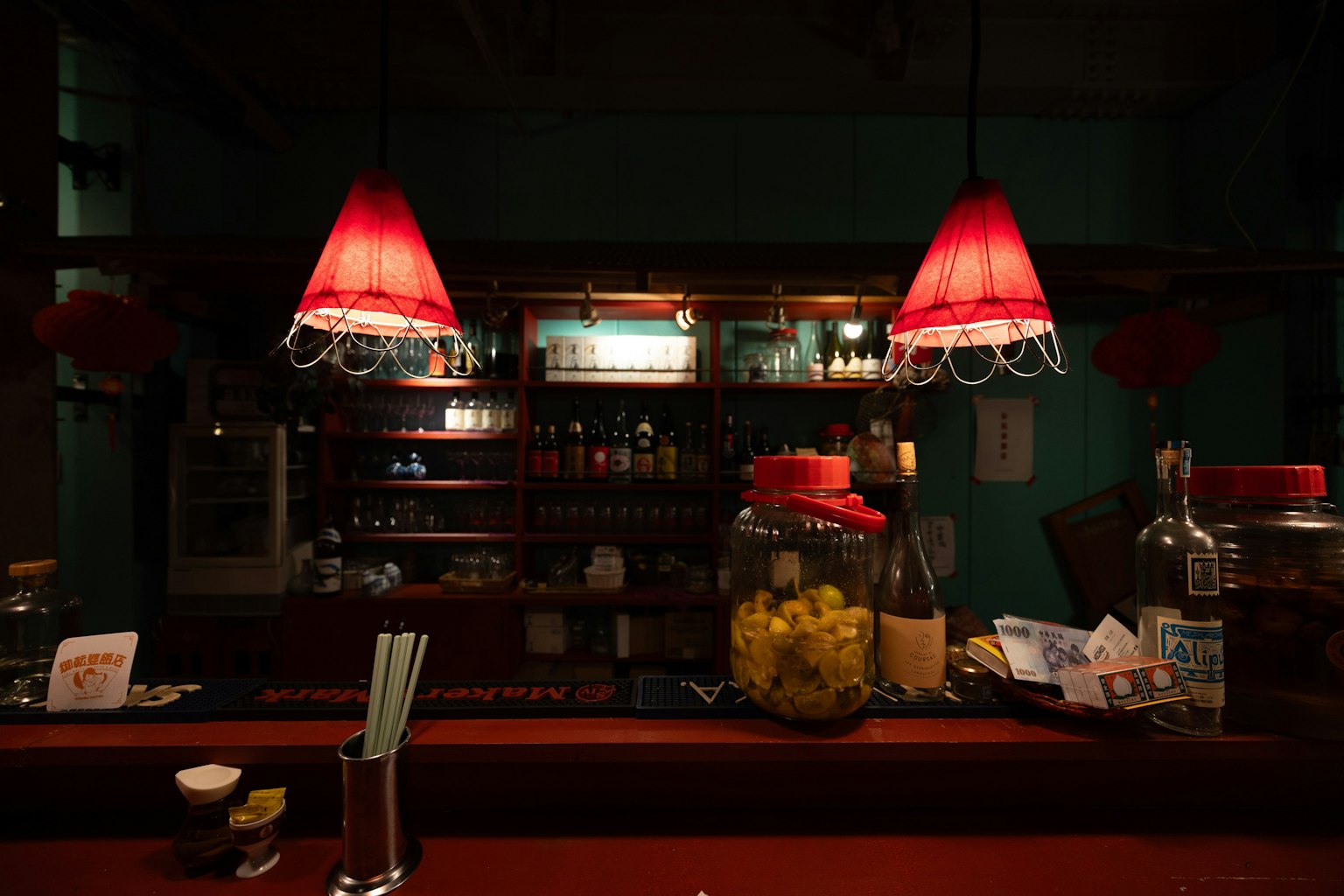 Intérieur d'un bar avec des lampes rouges suspendues au-dessus du comptoir et des étagères remplies de boissons