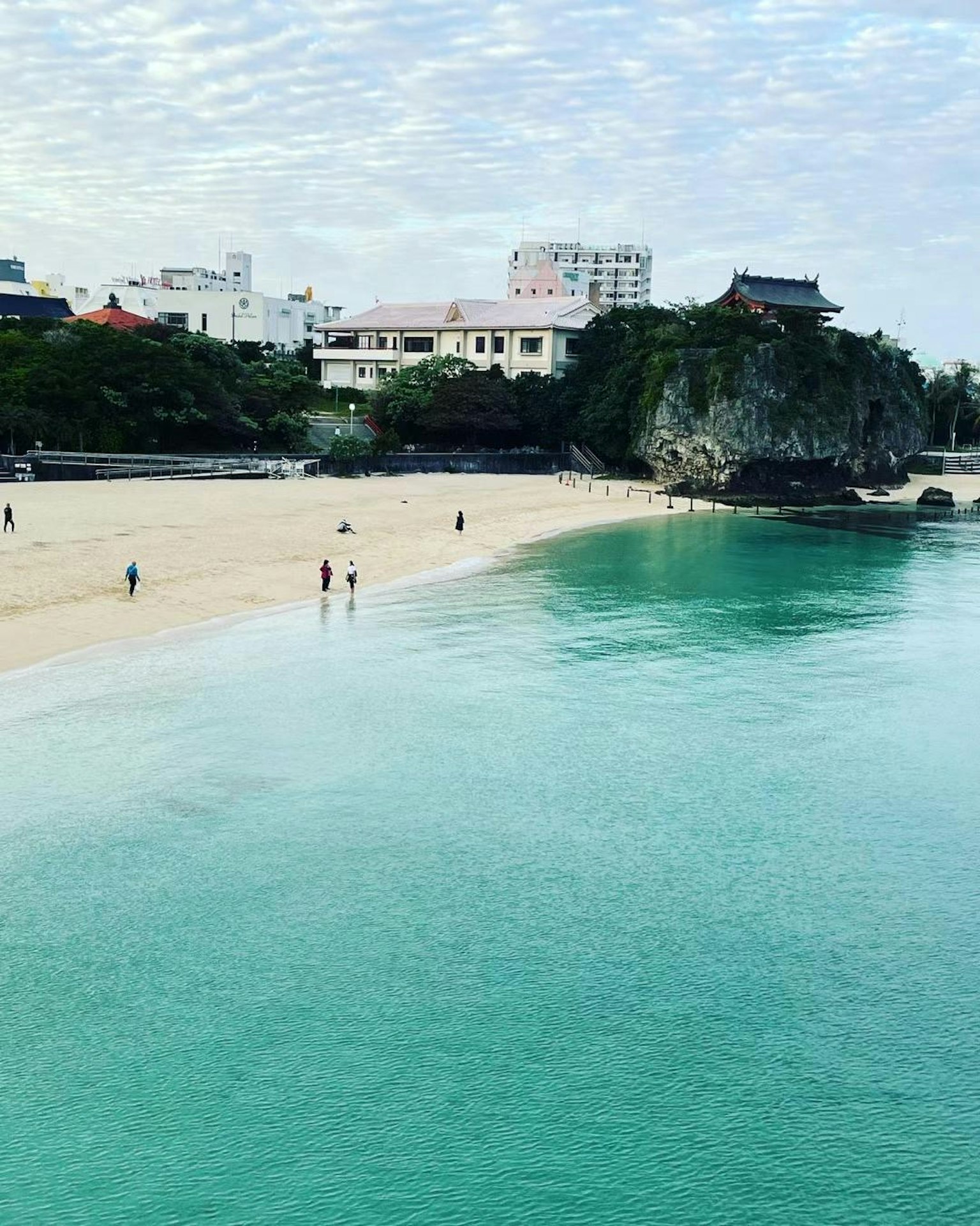 청록색 바다와 흰 모래가 있는 해변에서 사람들이 걷고 있음