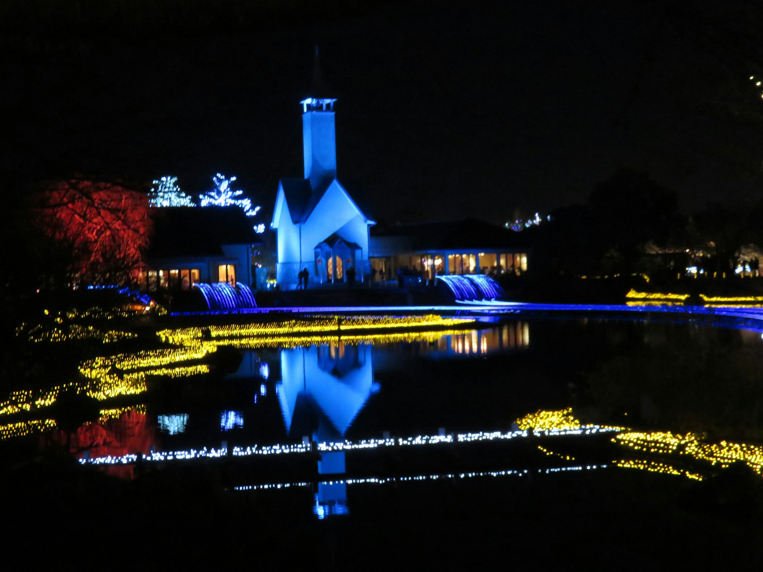 Scène magnifique d'une église illuminée en bleu la nuit avec un étang réfléchissant