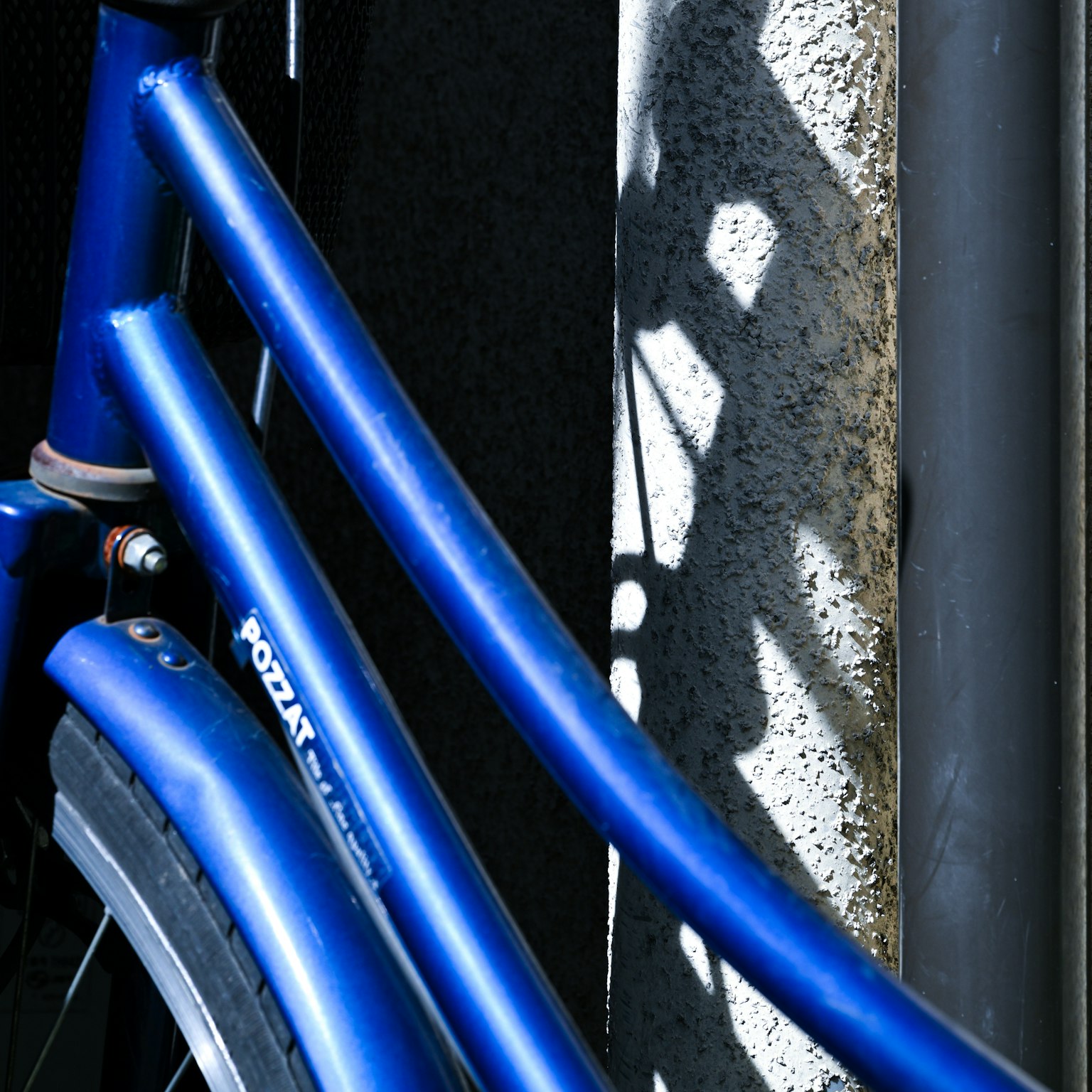 Nahaufnahme eines blauen Fahrradrahmens mit einem Schatten an einer Wand