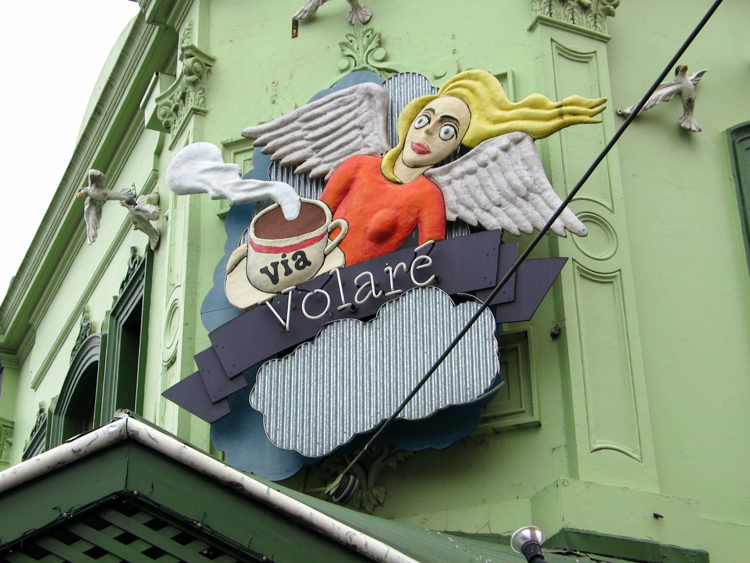 Schild mit einer geflügelten Frau an einem grünen Gebäude via Volare