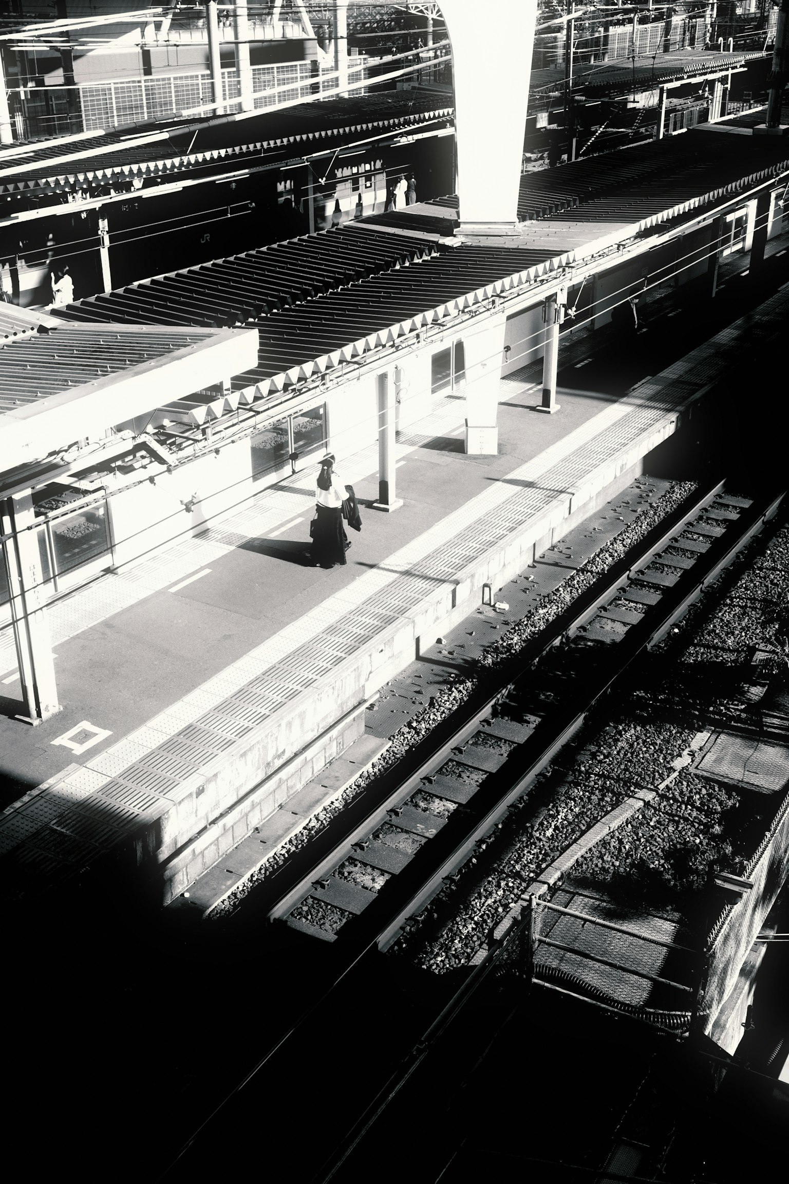 Gambar hitam putih dari platform stasiun kereta dengan rel yang terlihat seseorang berdiri di platform