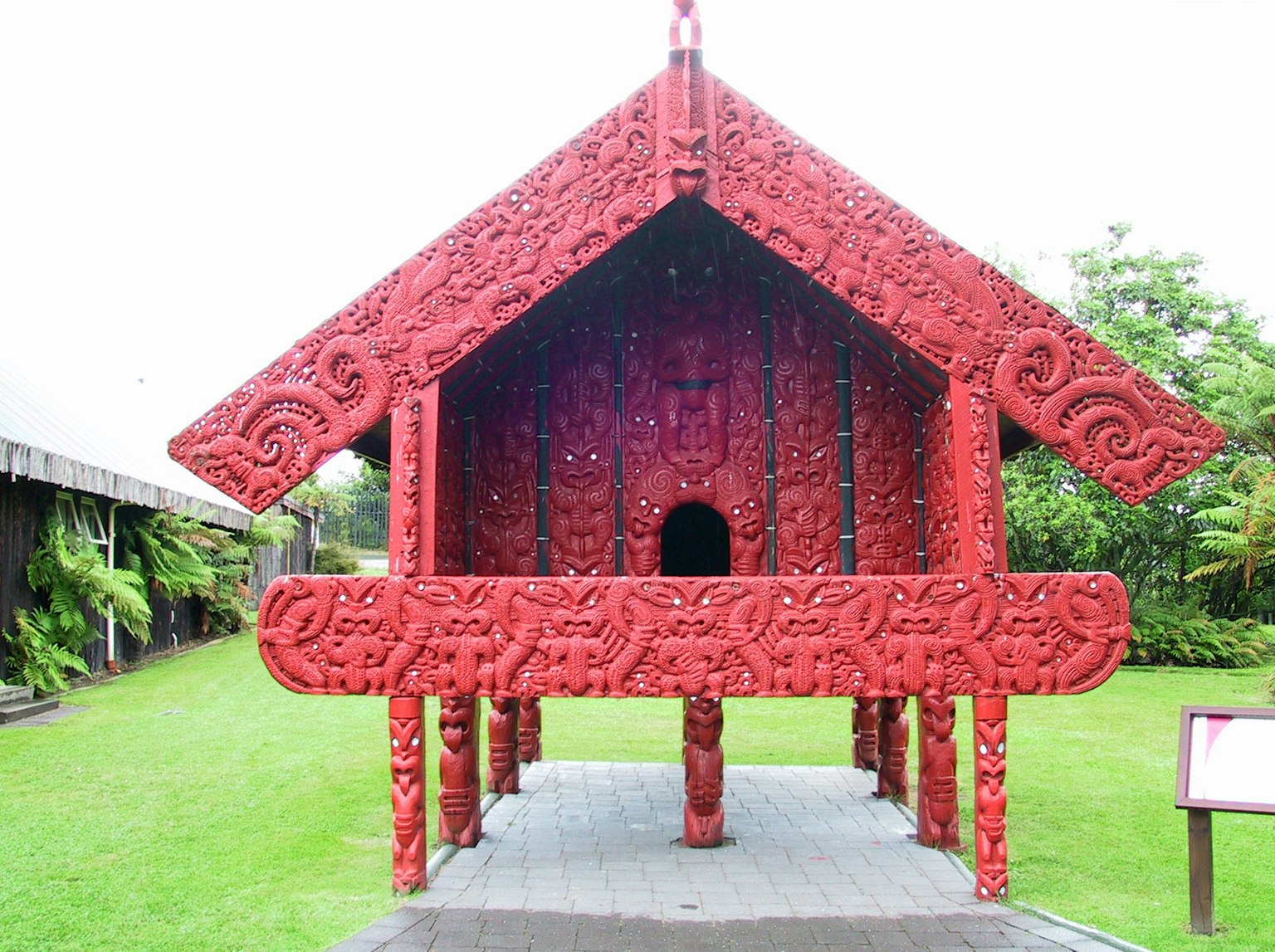 Pemandangan luar wharenui Maori dengan ukiran merah yang rumit