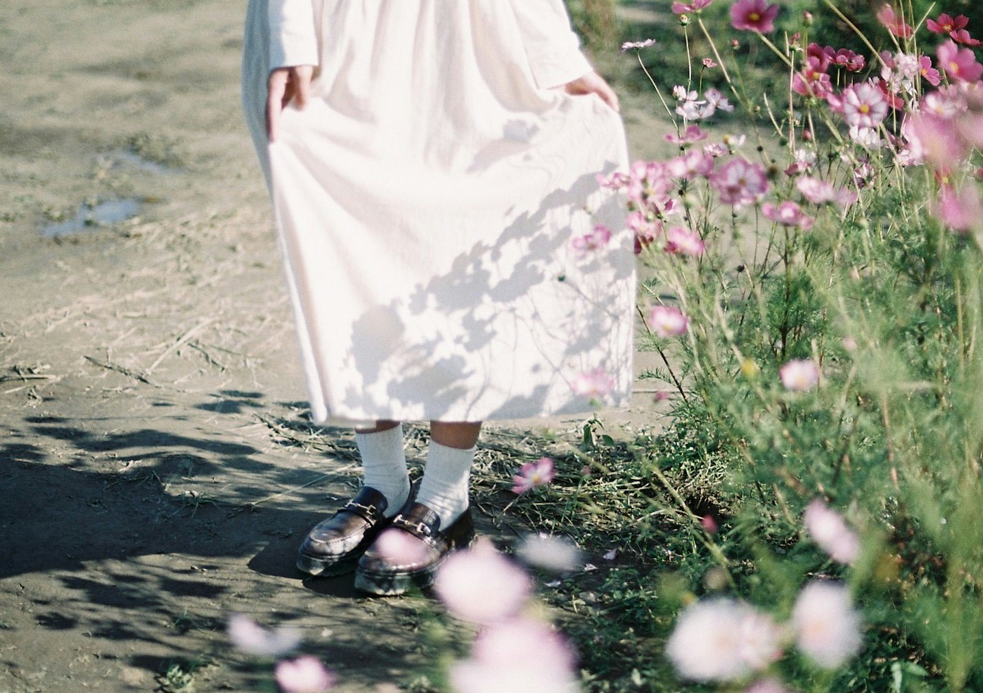 Person in weißem Kleid auf einem blumigen Pfad