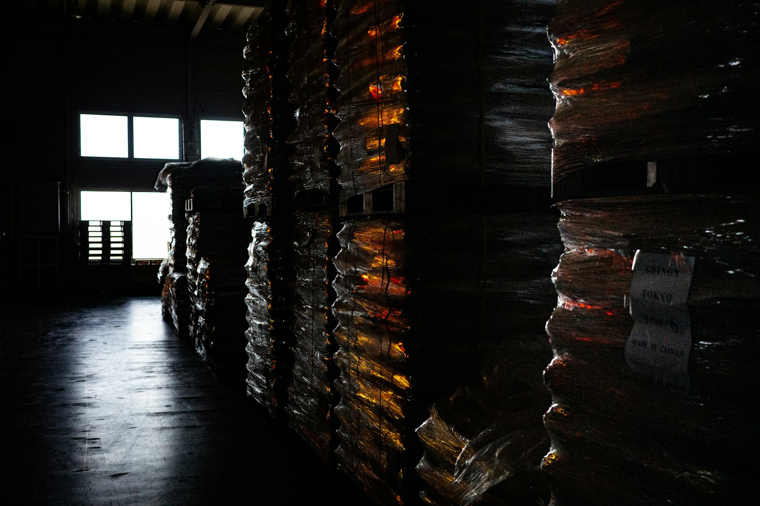 暗い倉庫内に積まれたパレットと窓からの微かな光