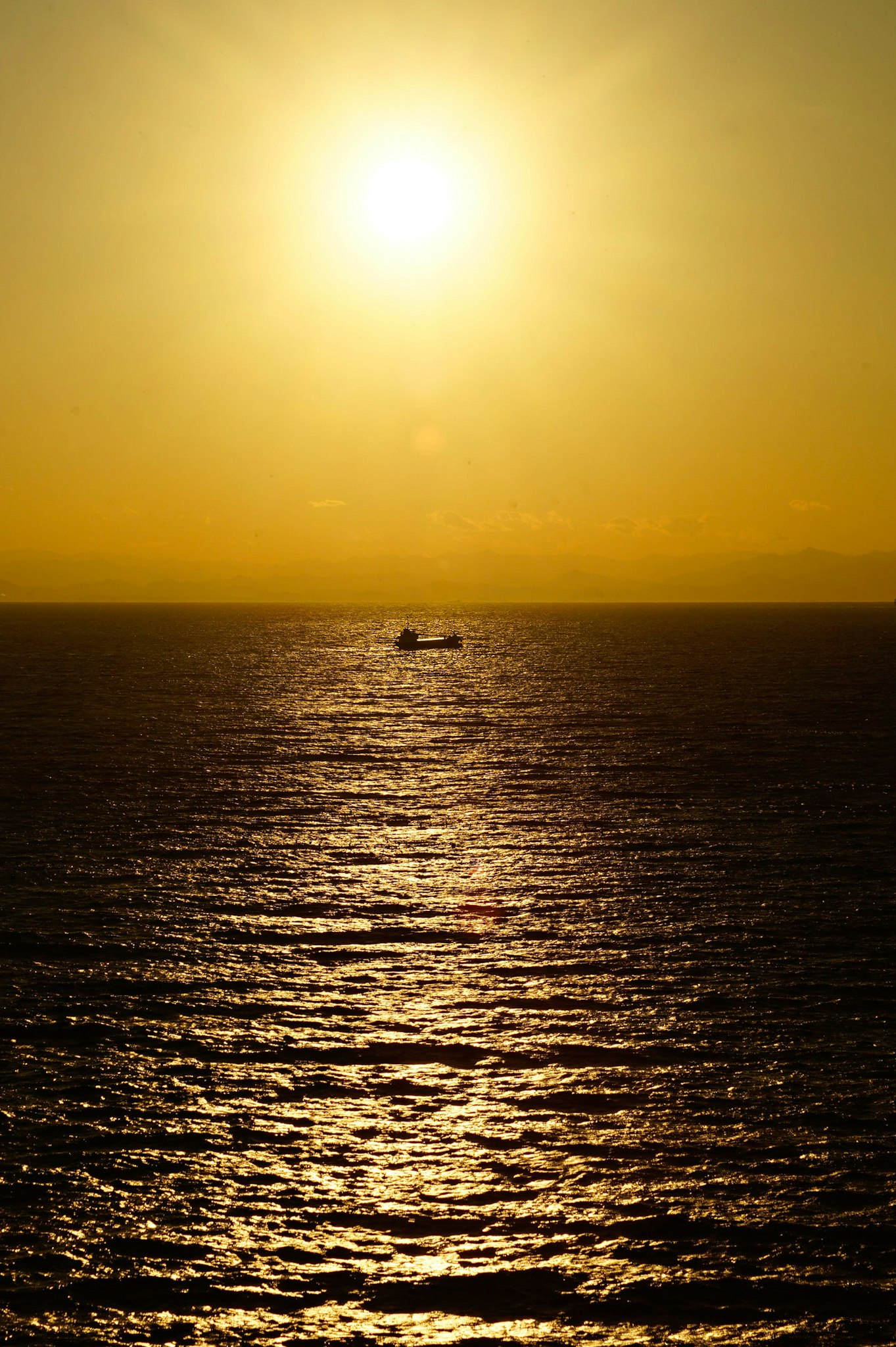 夕日に照らされた海面と水平線、船影のある風景