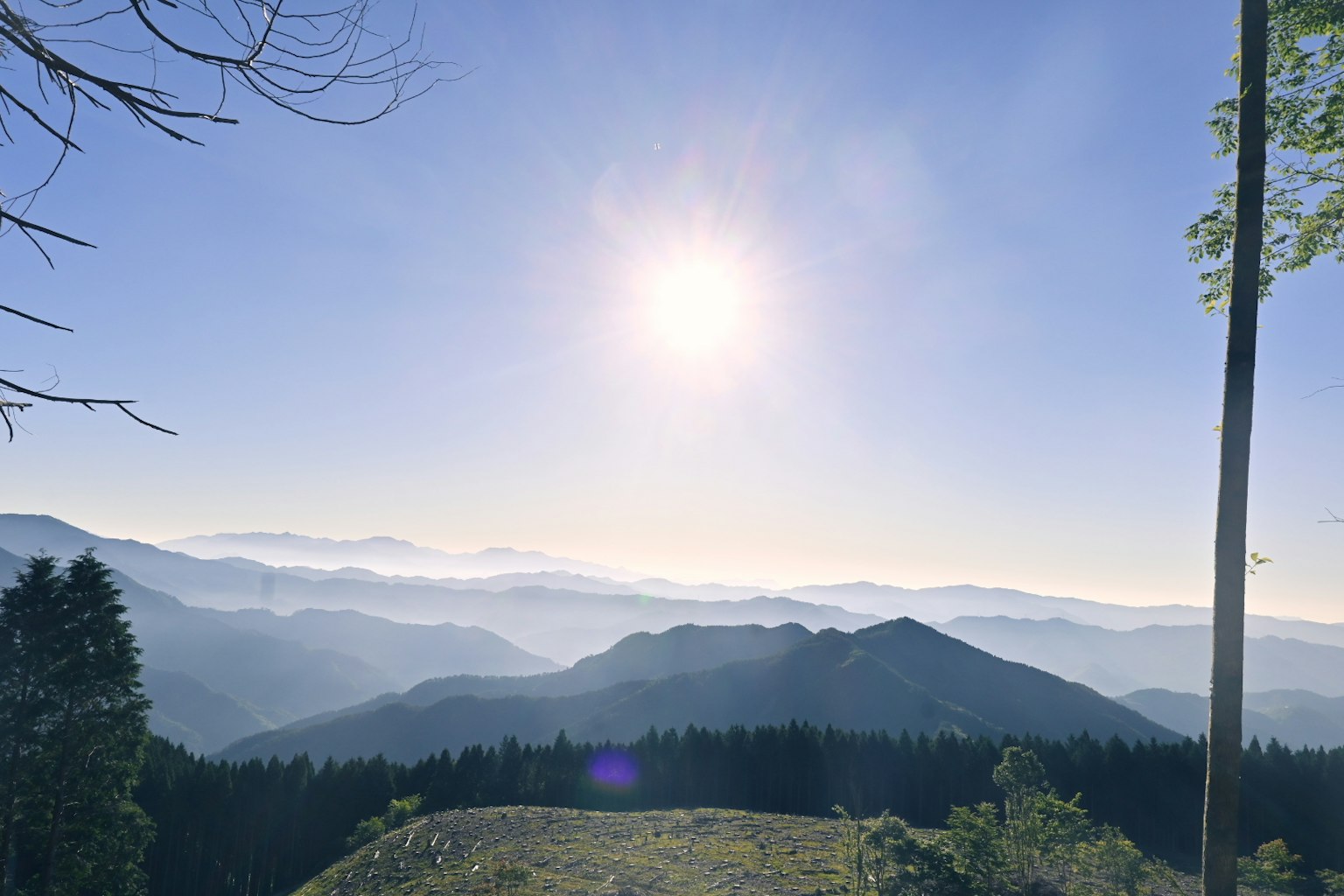 Vista panoramica delle montagne sotto un sole luminoso con cielo blu chiaro e valli nebbiose