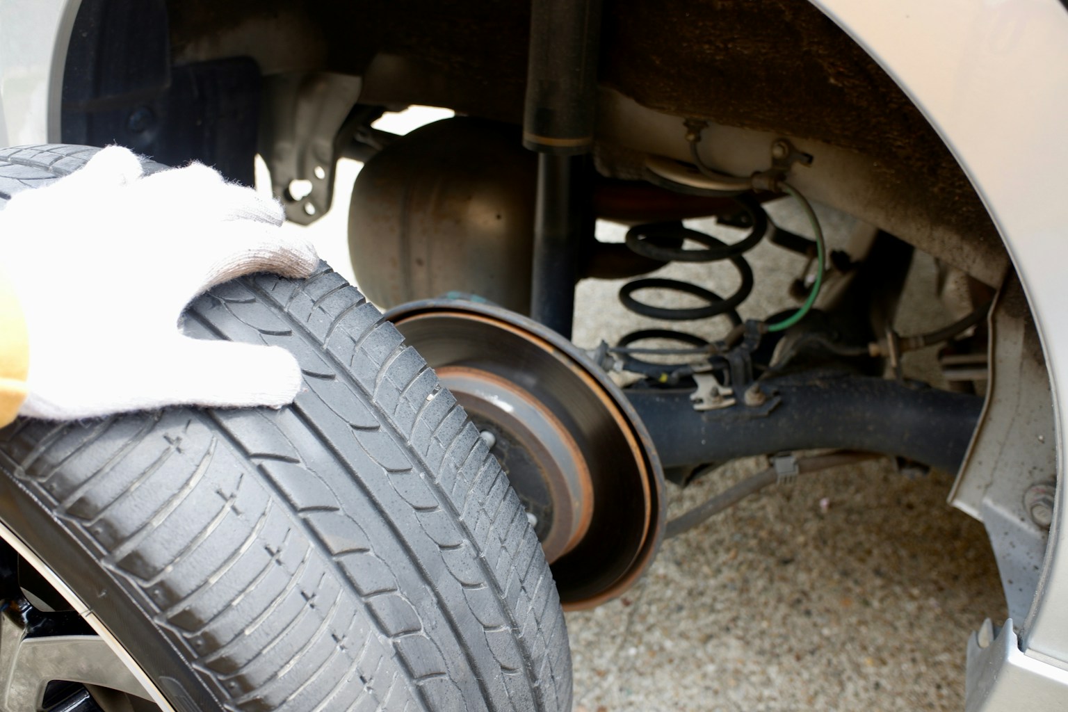 車のタイヤを持つ手とサスペンションの部品が見える