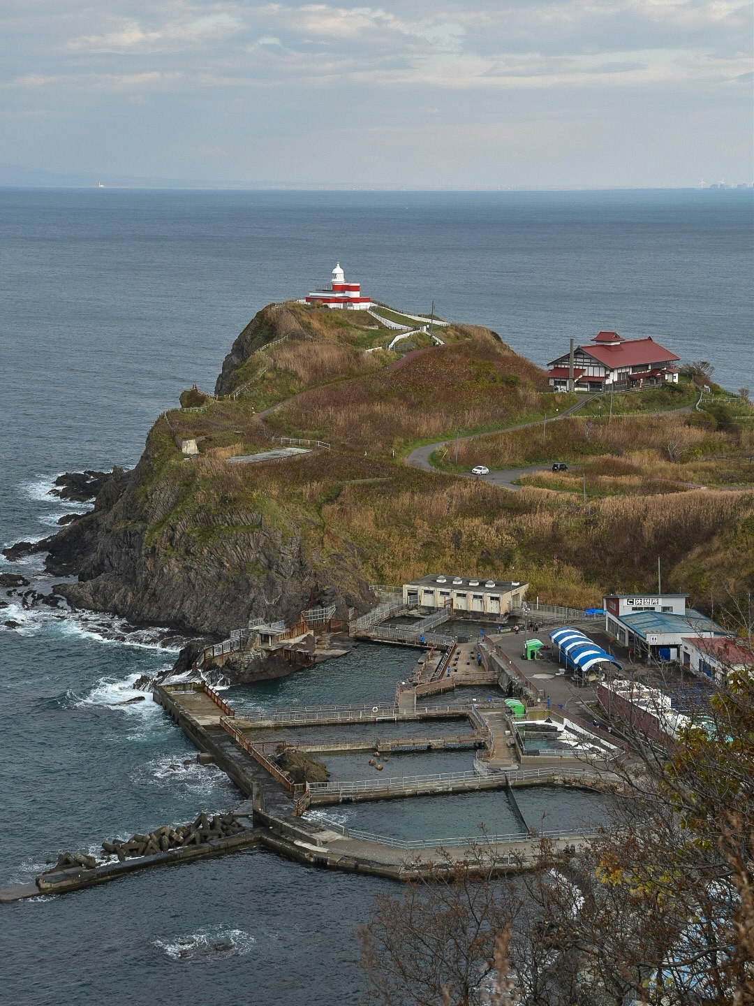 lighthouse and red-roof buildings on a rugged seaside cliff