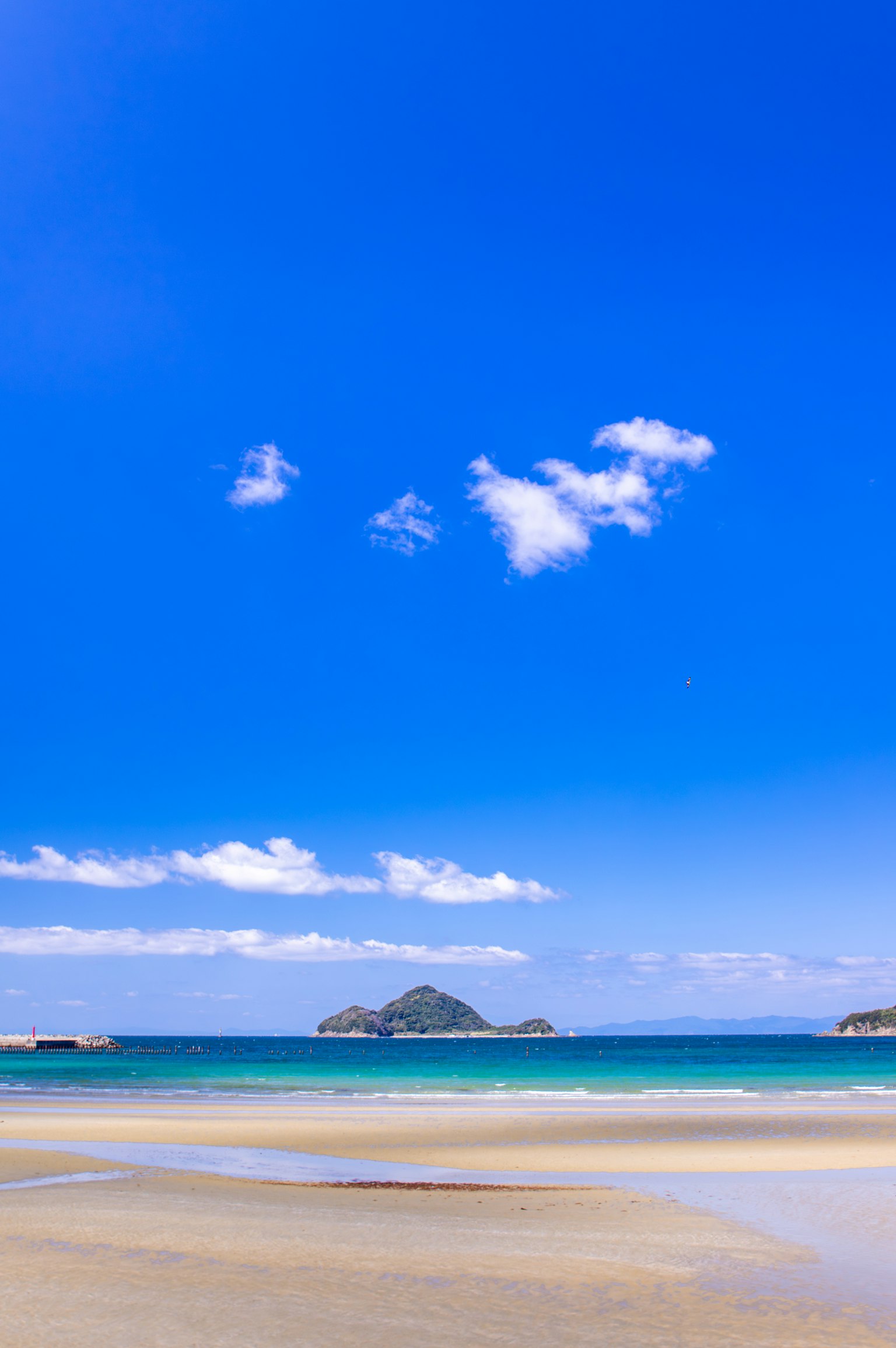 ทิวทัศน์ชายหาดที่สวยงามมีท้องฟ้าสีฟ้าและเมฆขาวเหนือทะเลที่สงบและชายหาดทราย