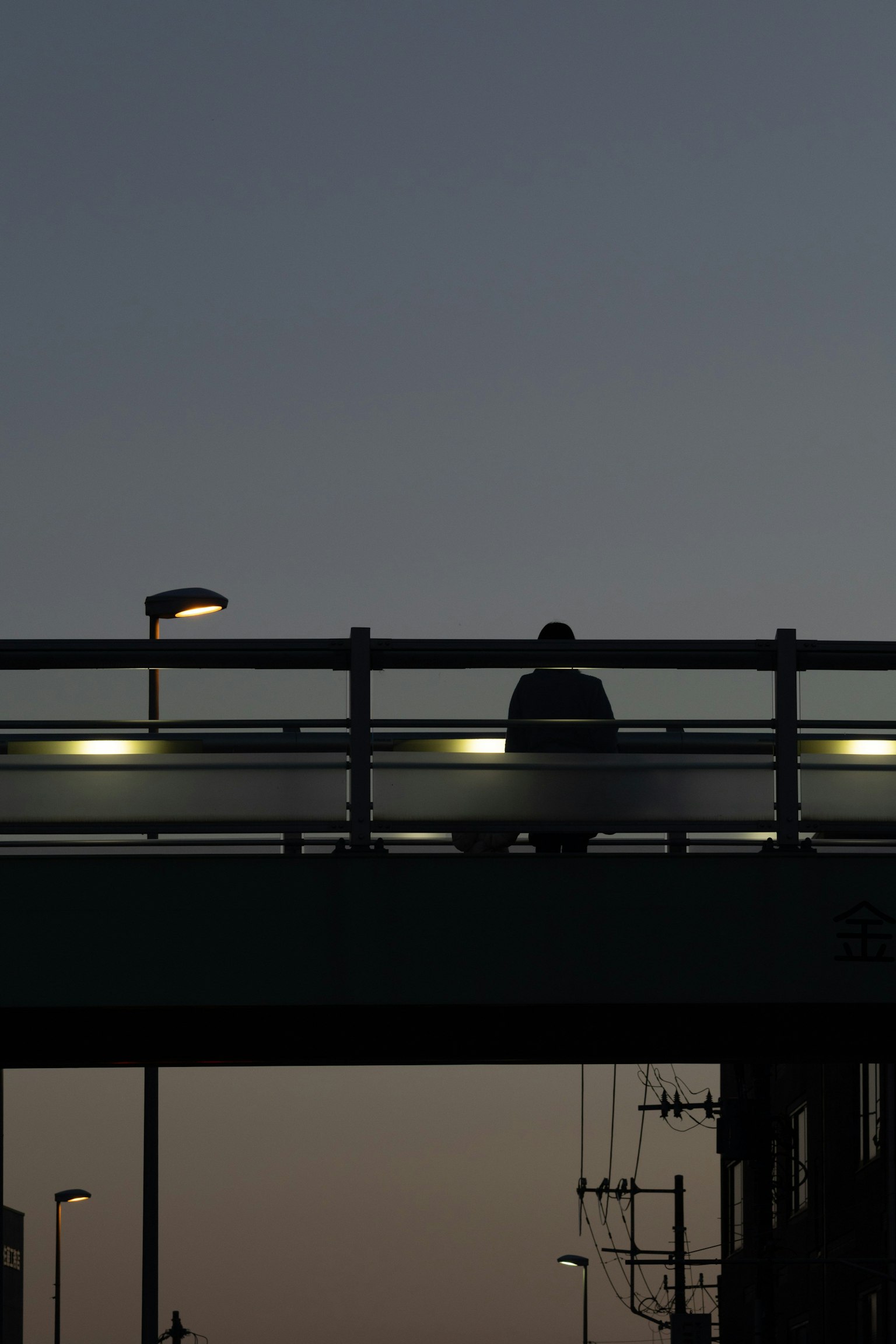 Silhouette of a person sitting on a bridge at dusk
