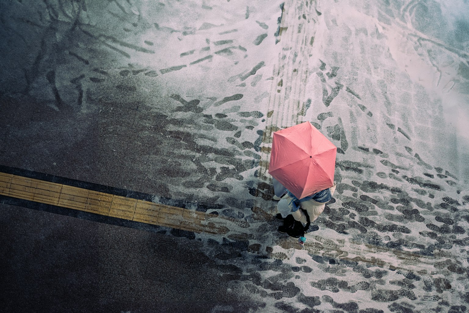 一個人手持粉紅色雨傘走在潮濕的人行道上