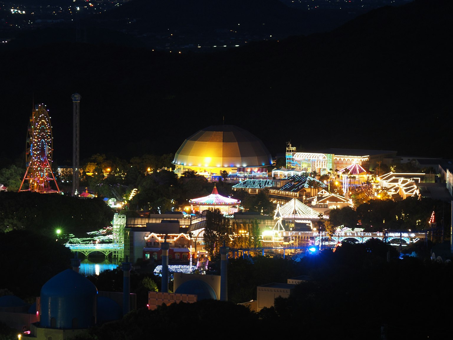 Vue nocturne d'un parc d'attractions avec une grande roue et un bâtiment en forme de dôme