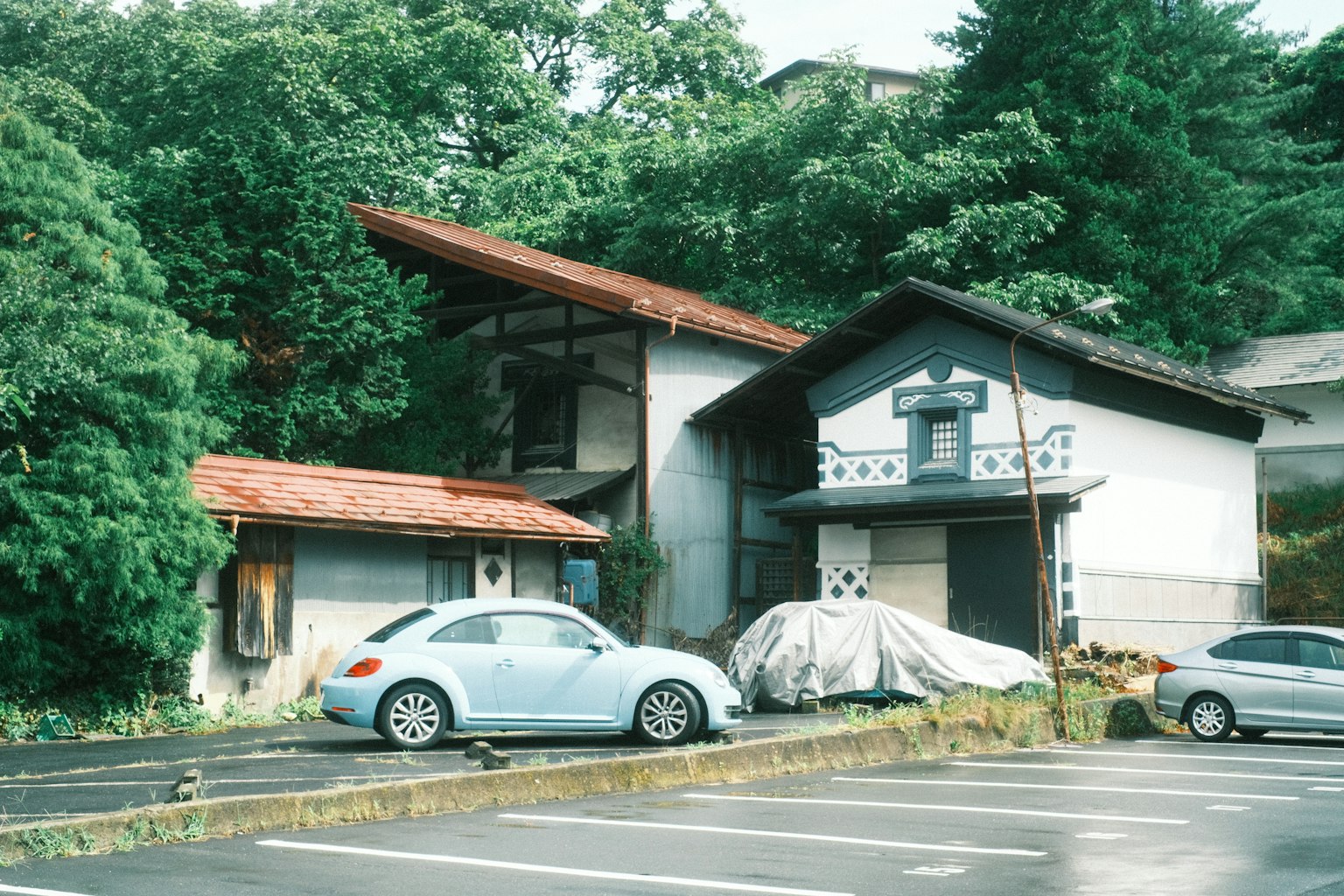 A scenic view featuring an old building and a blue car surrounded by green trees